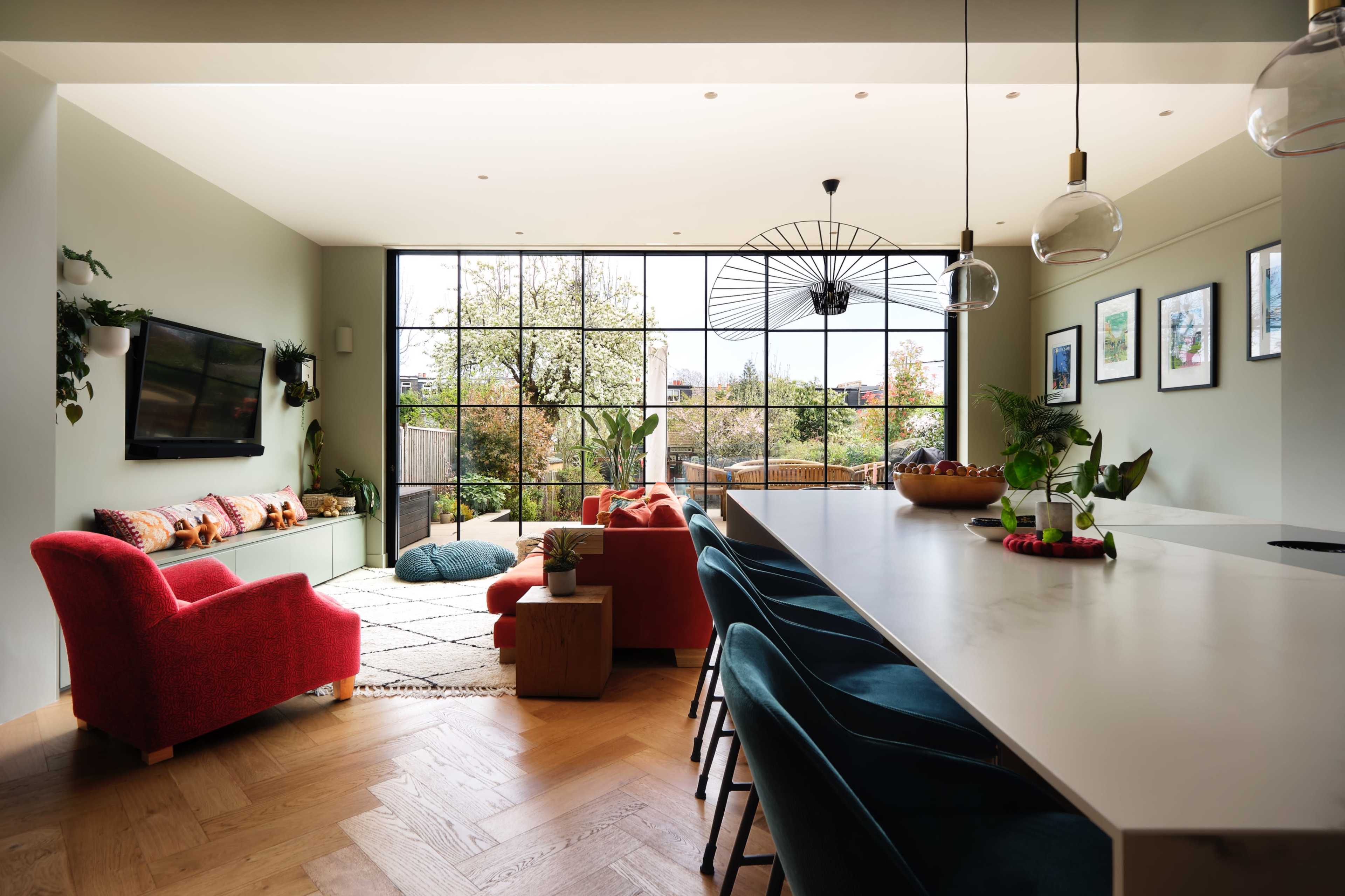 A modern living space features a large window with a view of greenery, a colorful seating area, and a sleek kitchen island with bar stools.
