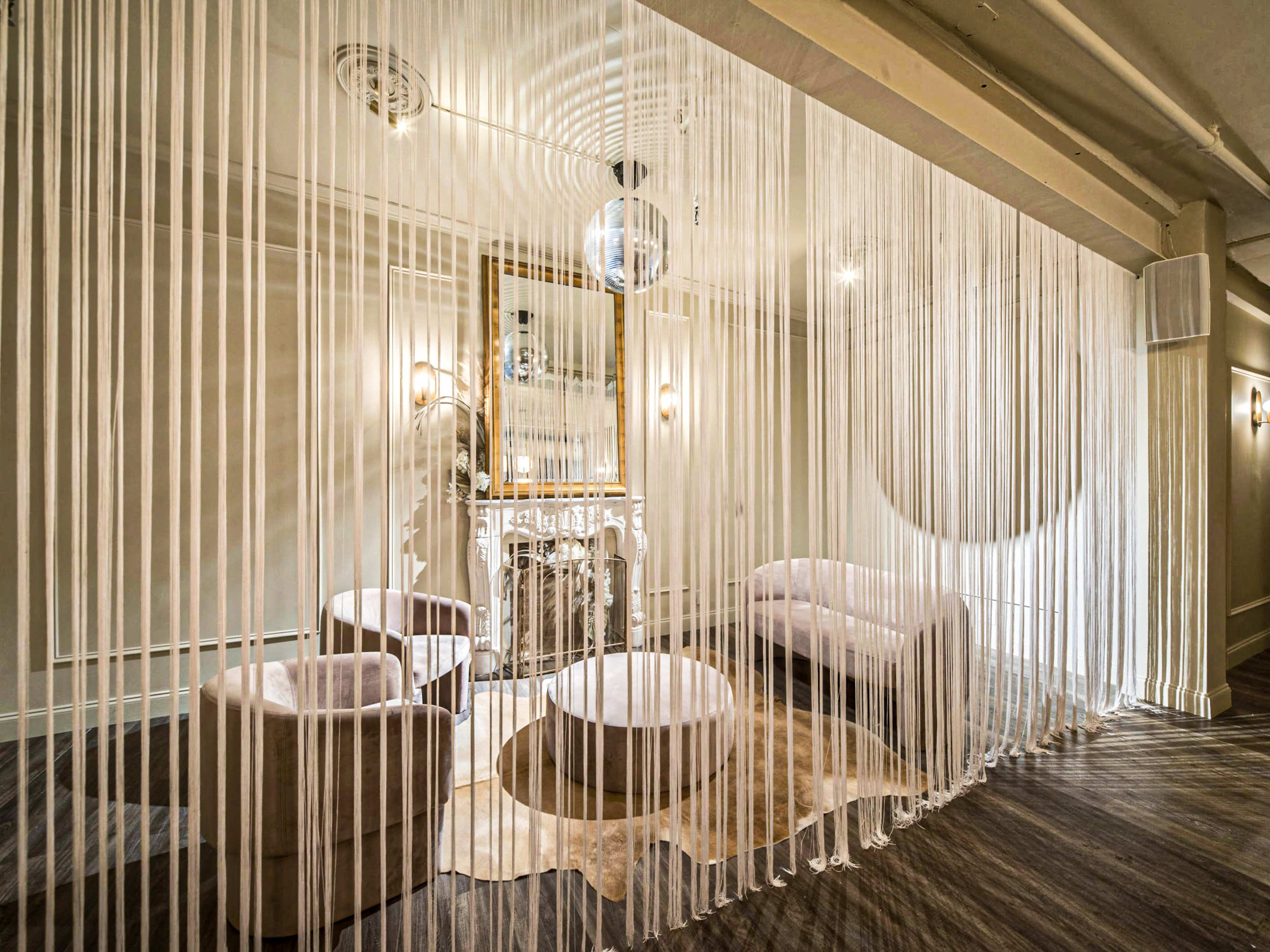A stylish room divided by long, sheer curtains with modern furniture, including two sofas and a round table, set against a decorative fireplace.