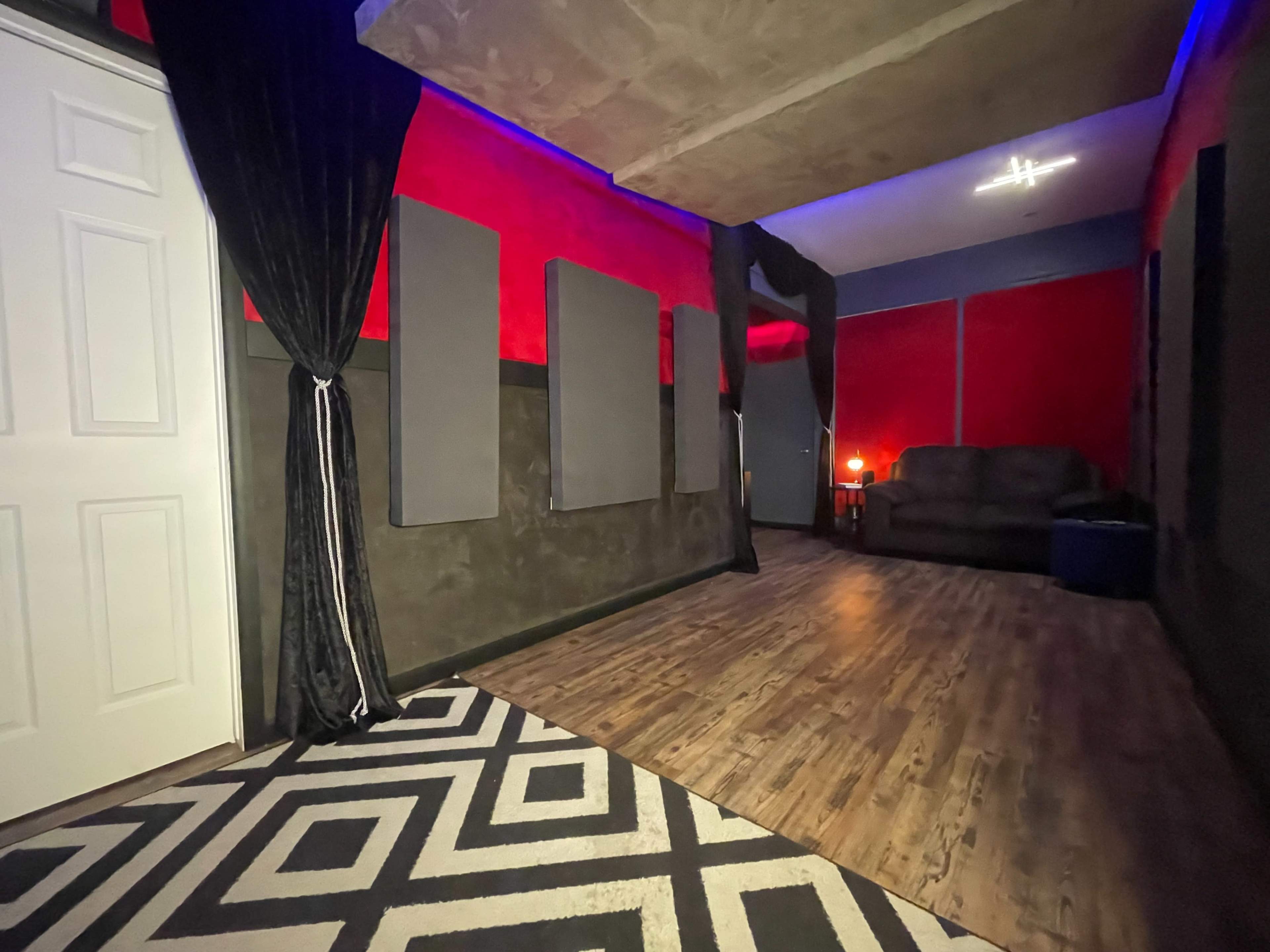 A room with red walls, acoustic panels, a dark couch, and a patterned rug.