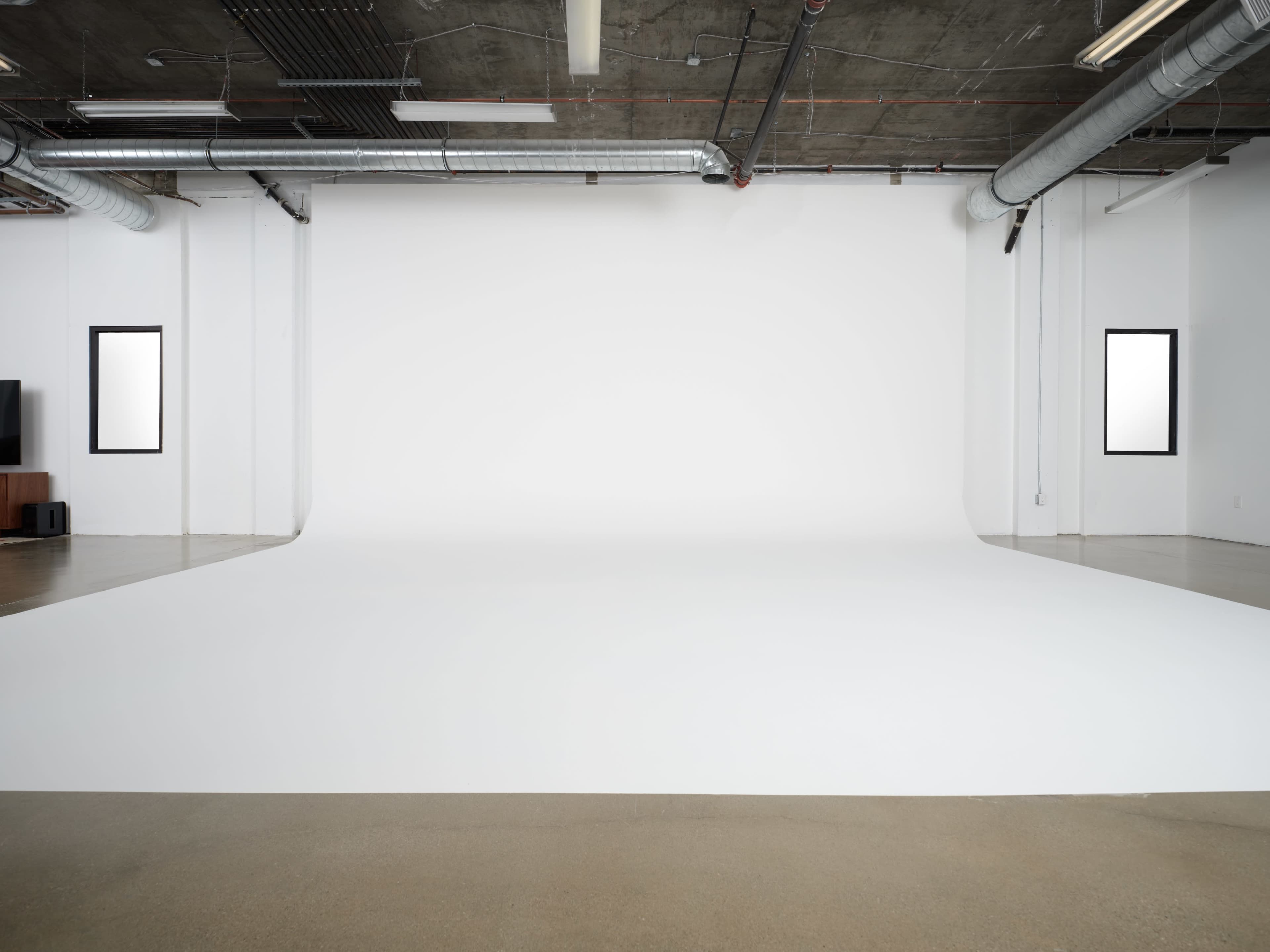 A spacious, empty studio with a seamless white backdrop and concrete flooring.