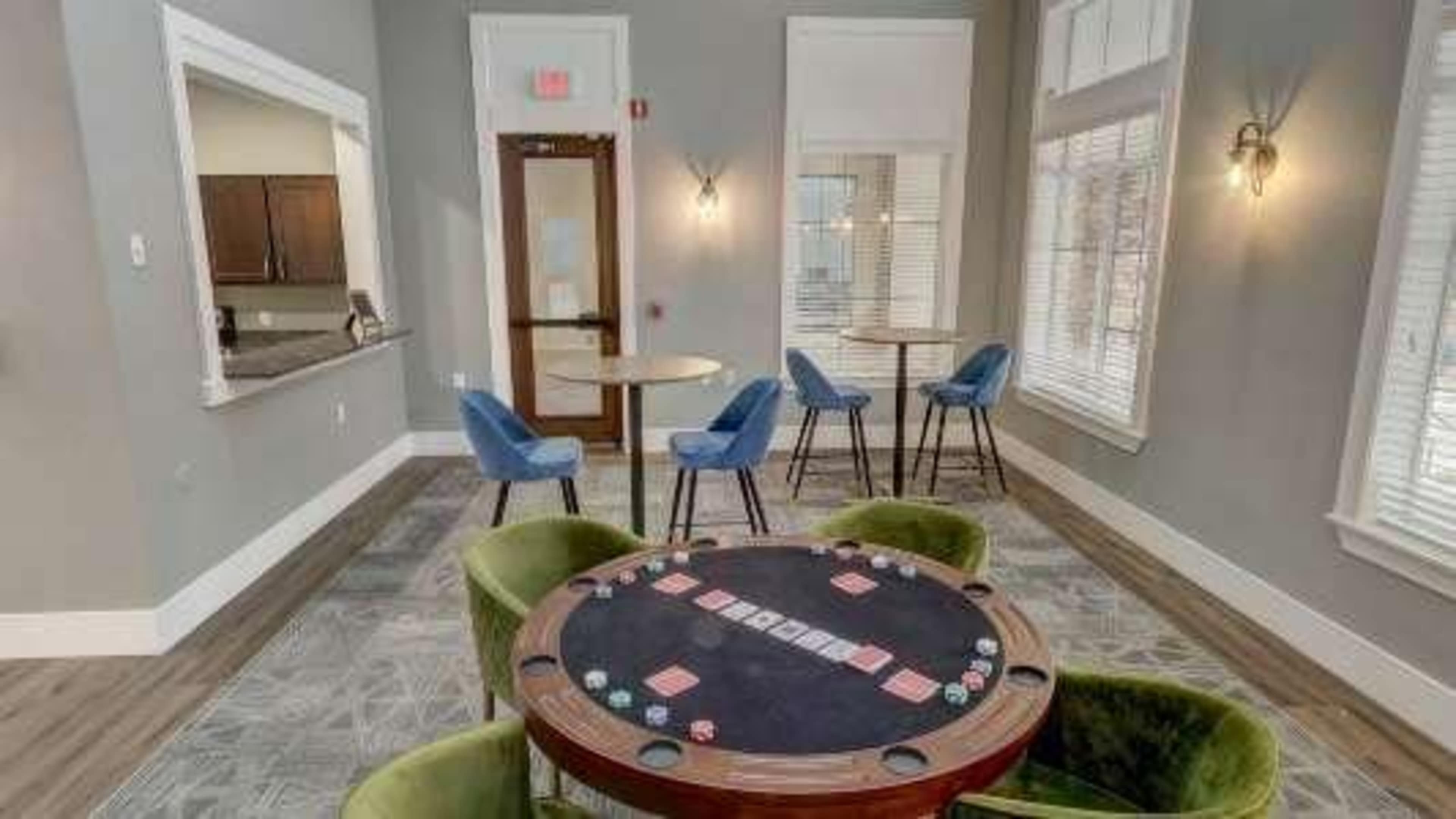 A well-lit room featuring a round poker table with gaming chips, surrounded by four chairs and two additional tables with blue seating.