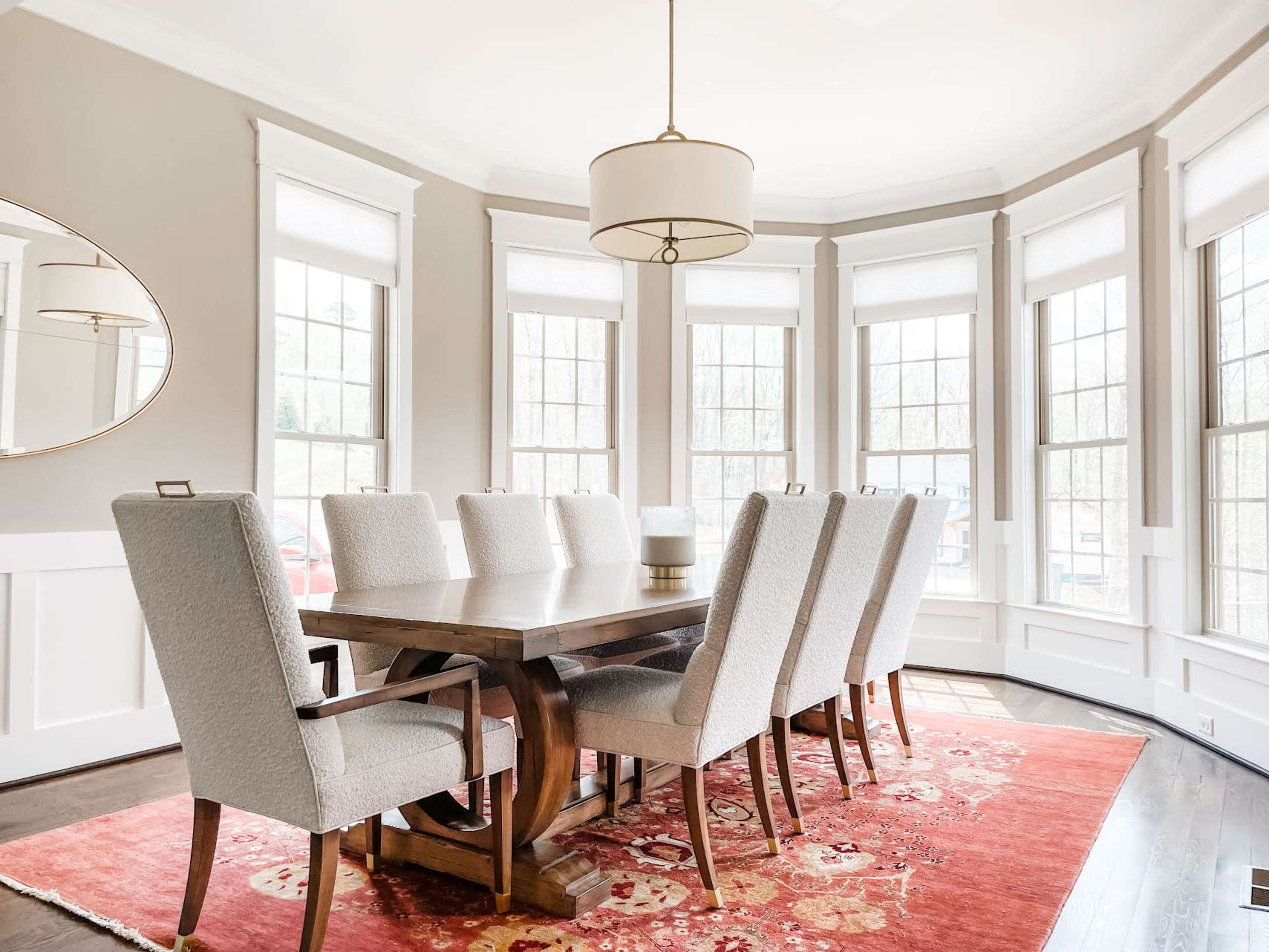 A well-furnished dining room features a large wooden table surrounded by upholstered chairs, with ample natural light streaming in through multiple windows.