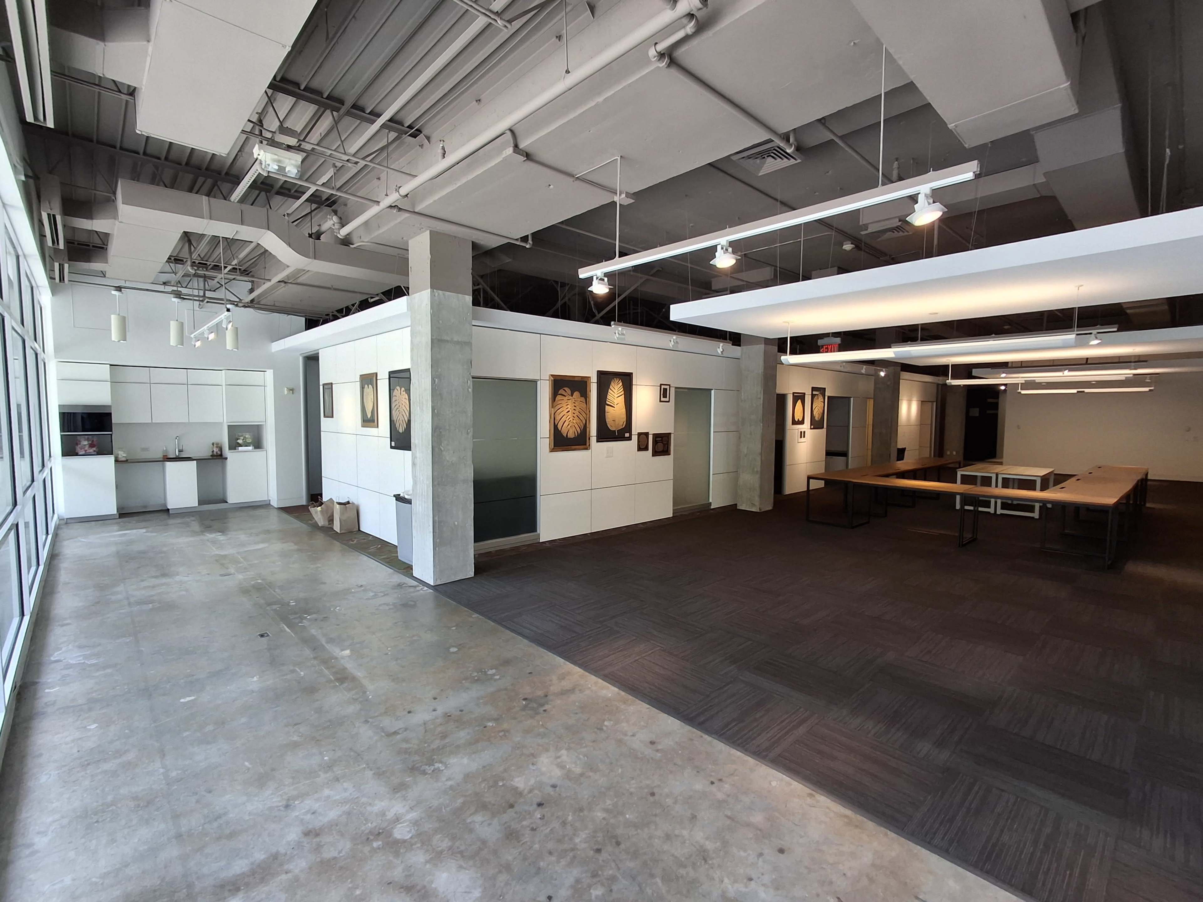 The image shows a spacious, modern office area with white walls, a dark carpeted section, and several artwork pieces displayed.