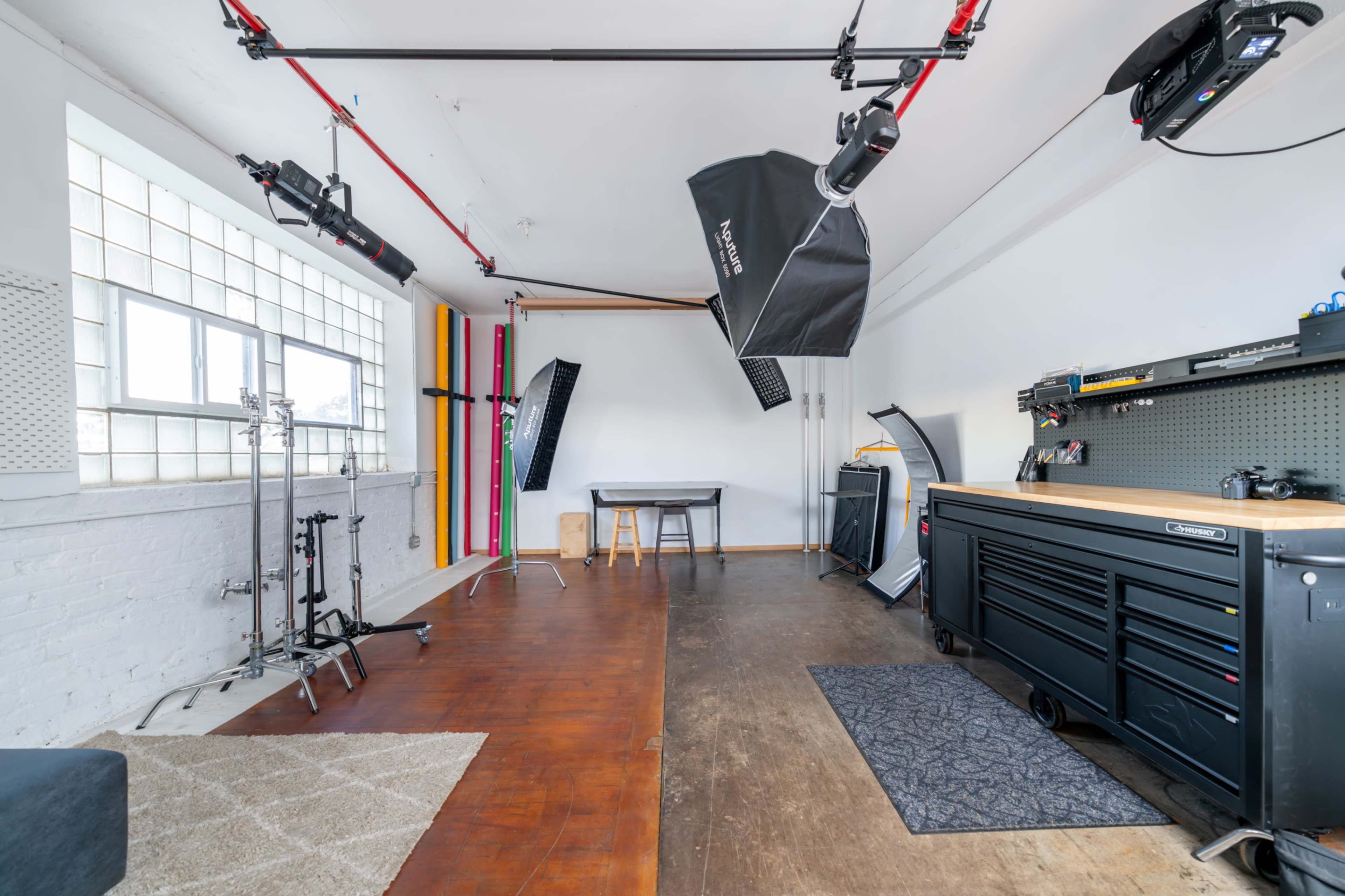 The image shows a photography studio with various lighting equipment, a table, and a workbench against a wall with pegboards.