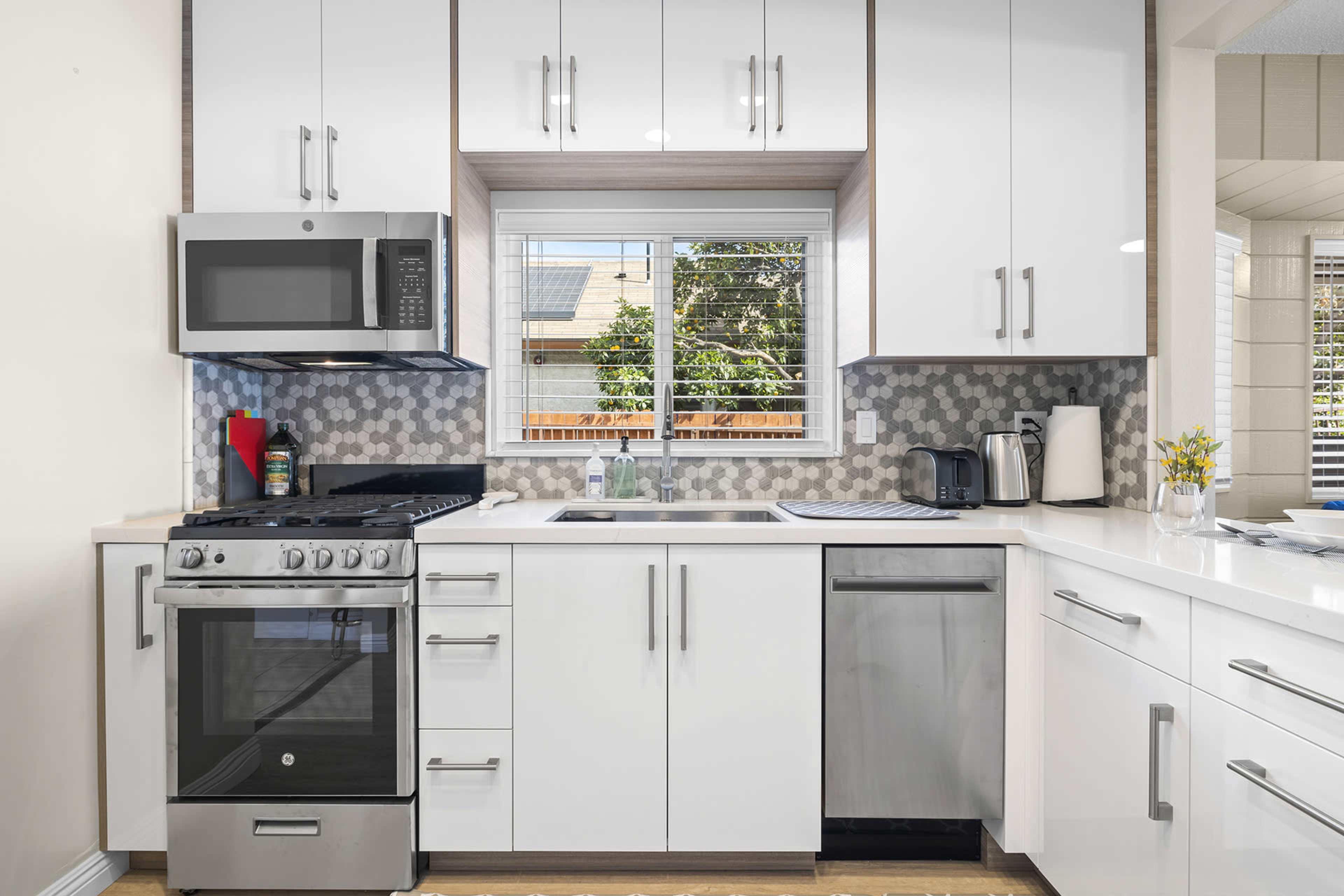 A modern kitchen featuring stainless steel appliances, white cabinetry, and a window overlooking a garden.
