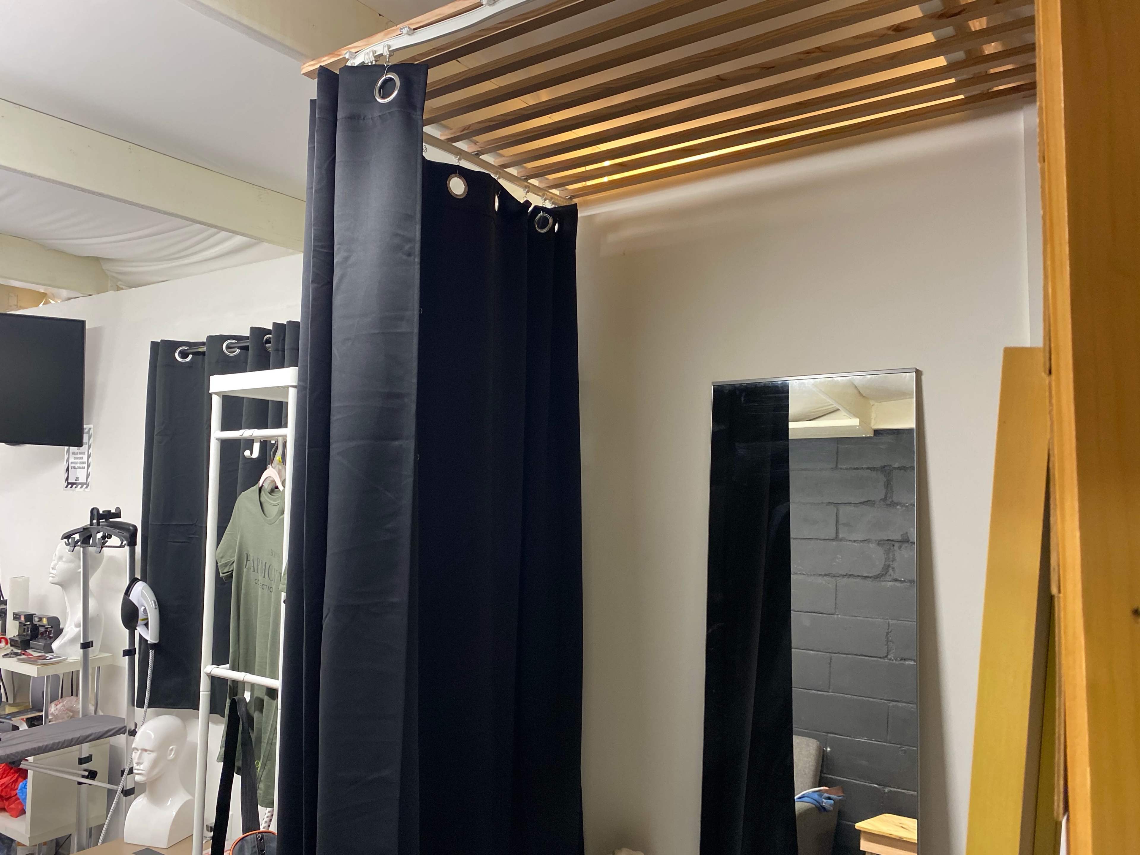 A room features a wooden slat ceiling above a black curtain area, with a mirror and various items arranged nearby.