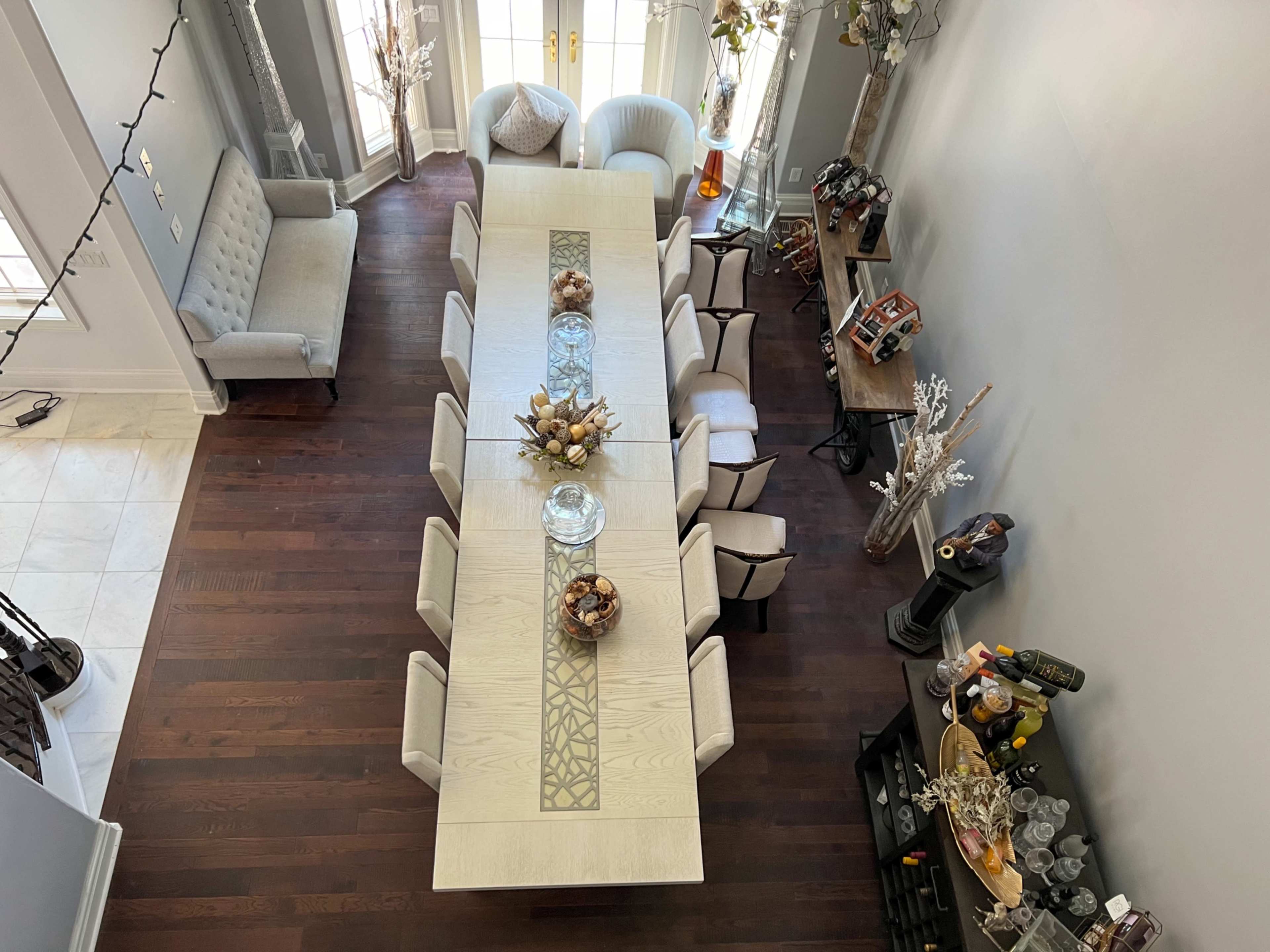 A large dining table with twelve chairs is set in a brightly lit room, surrounded by a couch and decorative elements.