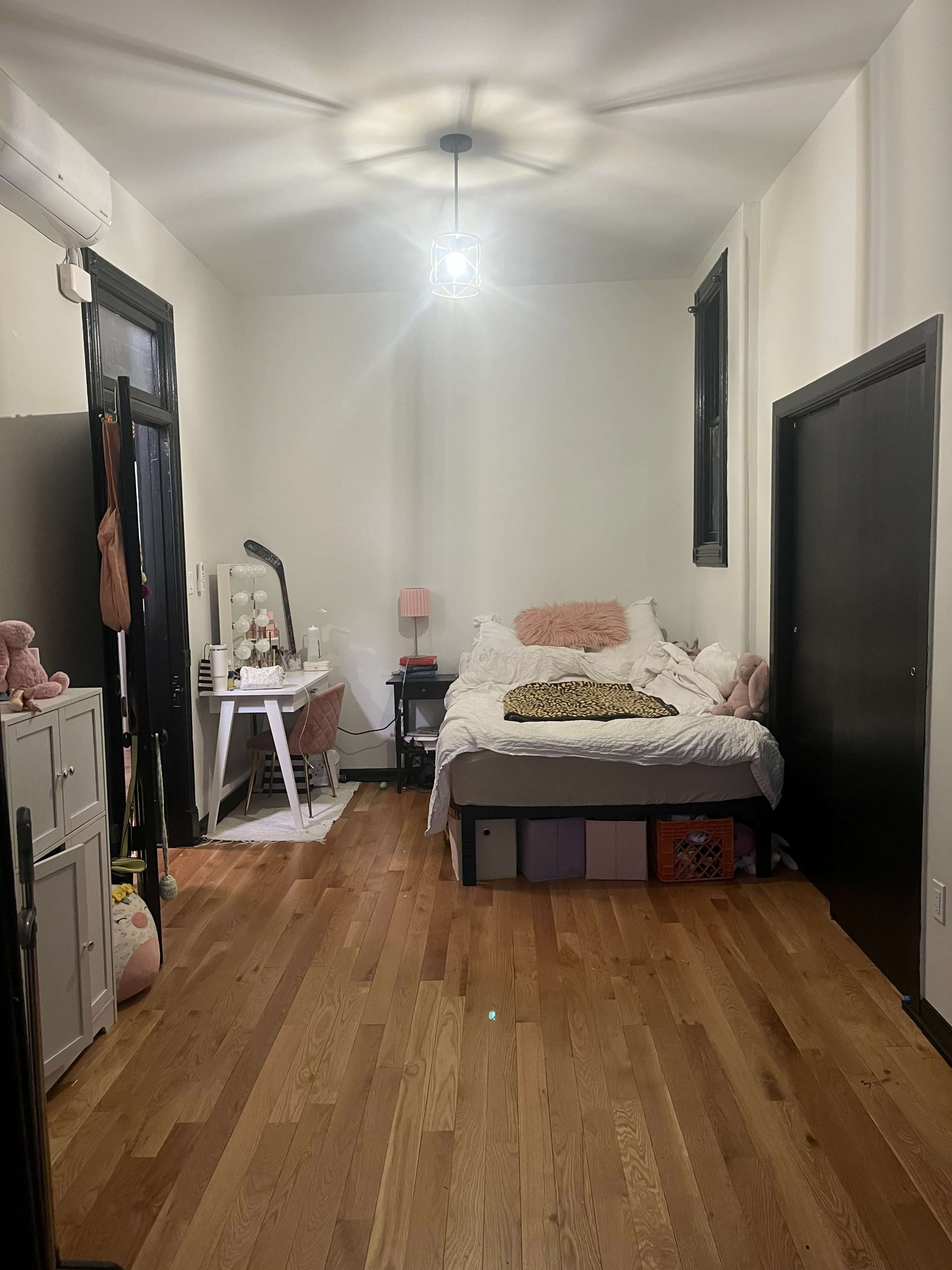 The image shows a tidy bedroom with a bed, a desk, and wooden flooring.