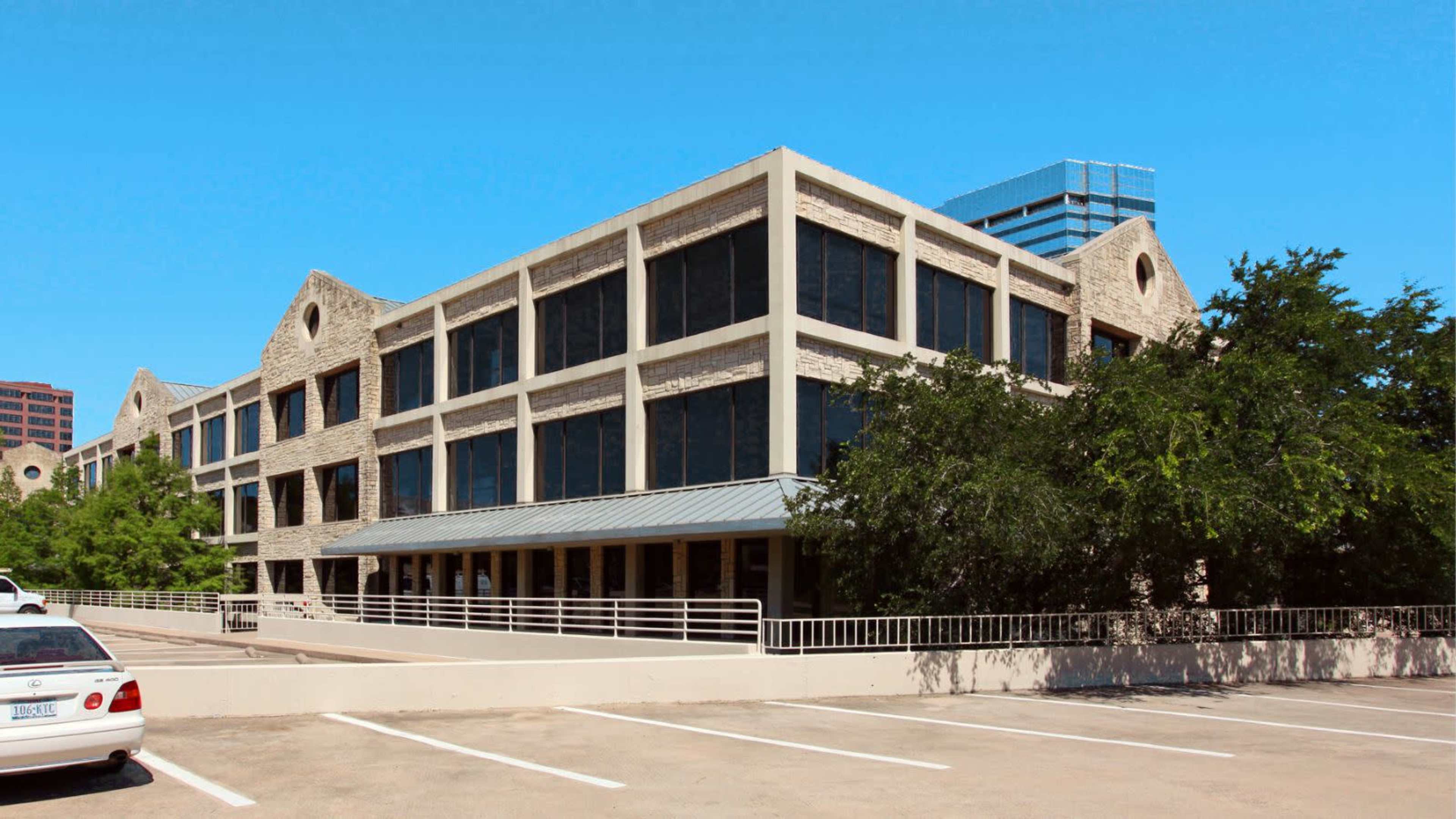 A modern, two-story stone and concrete building with large windows and parking space in front.