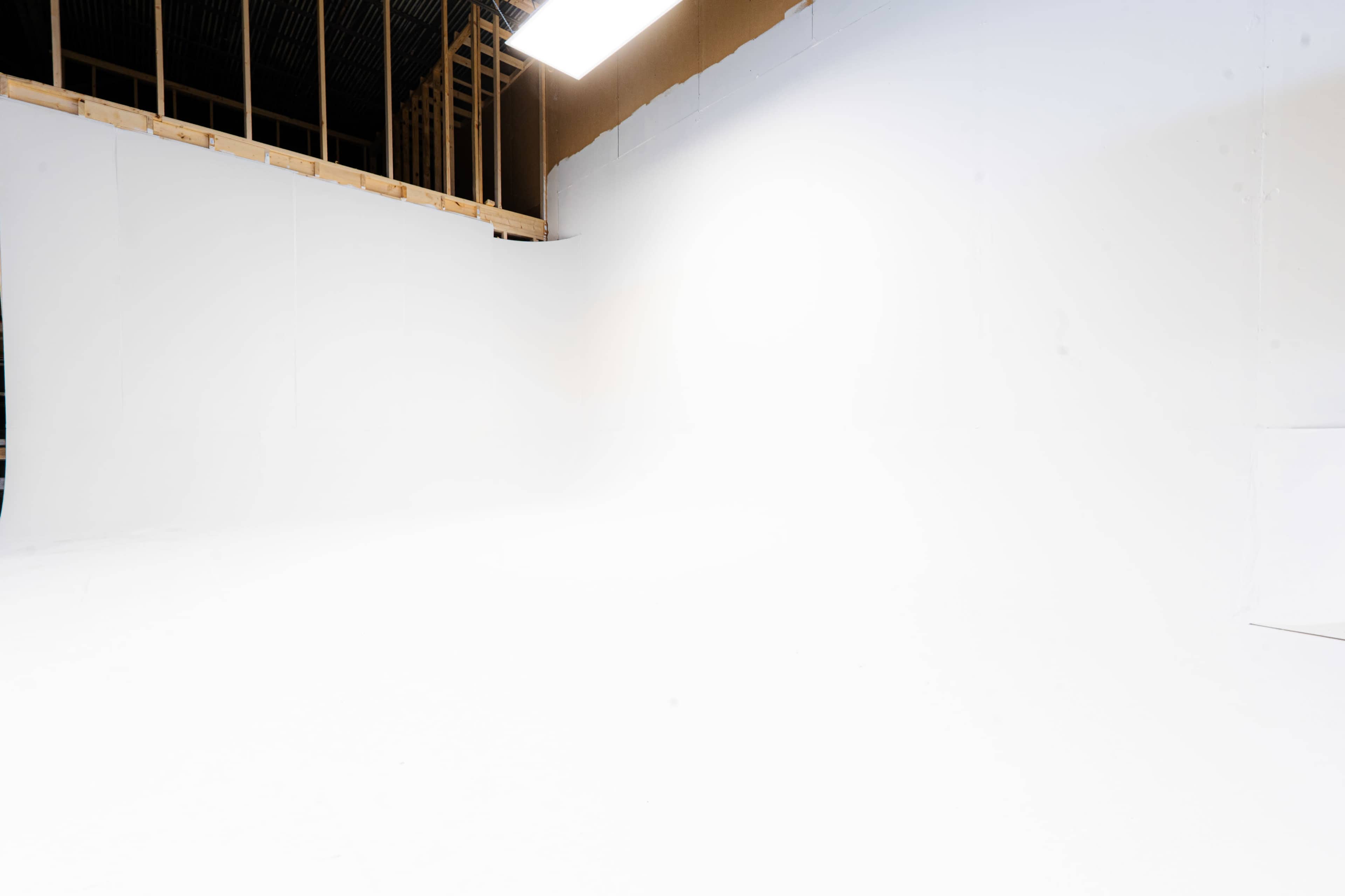 A large empty studio space features white walls and a smooth floor, with exposed wooden beams visible in the upper part of the room.