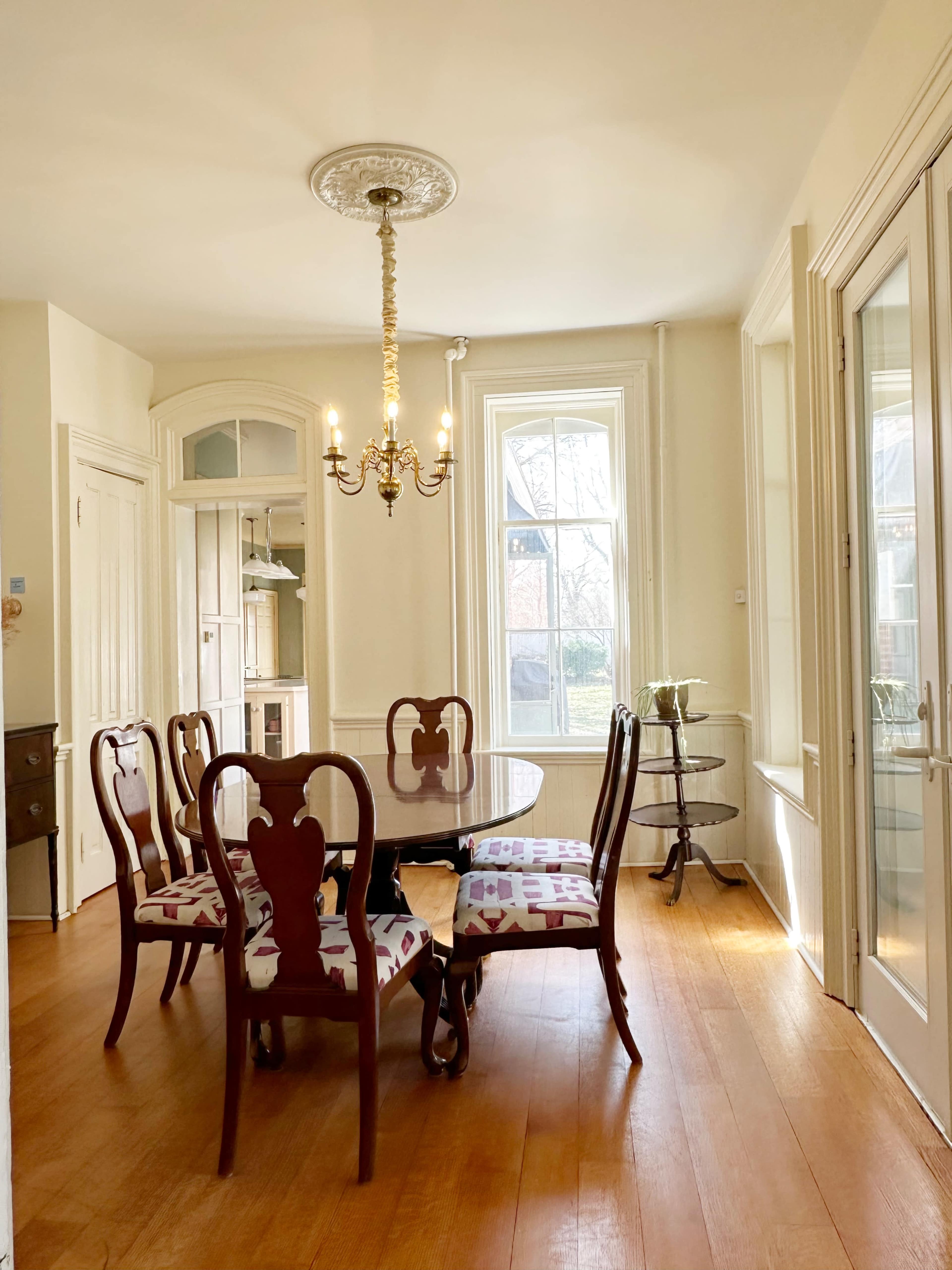 A dining area features a round table surrounded by six chairs with patterned upholstery, illuminated by a chandelier hanging from the ceiling.