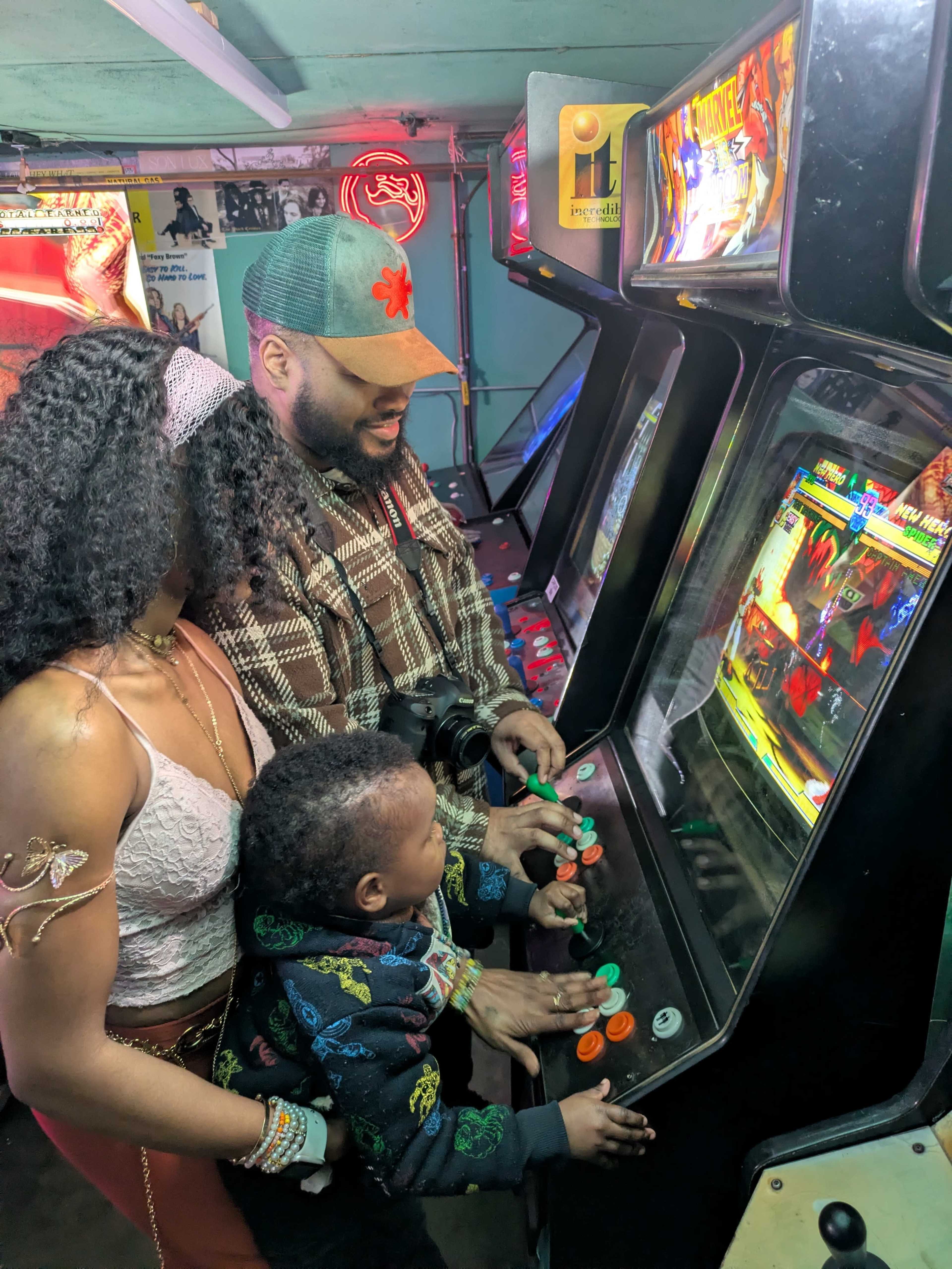 A family enjoys playing classic arcade games together in an arcade filled with colorful lights.
