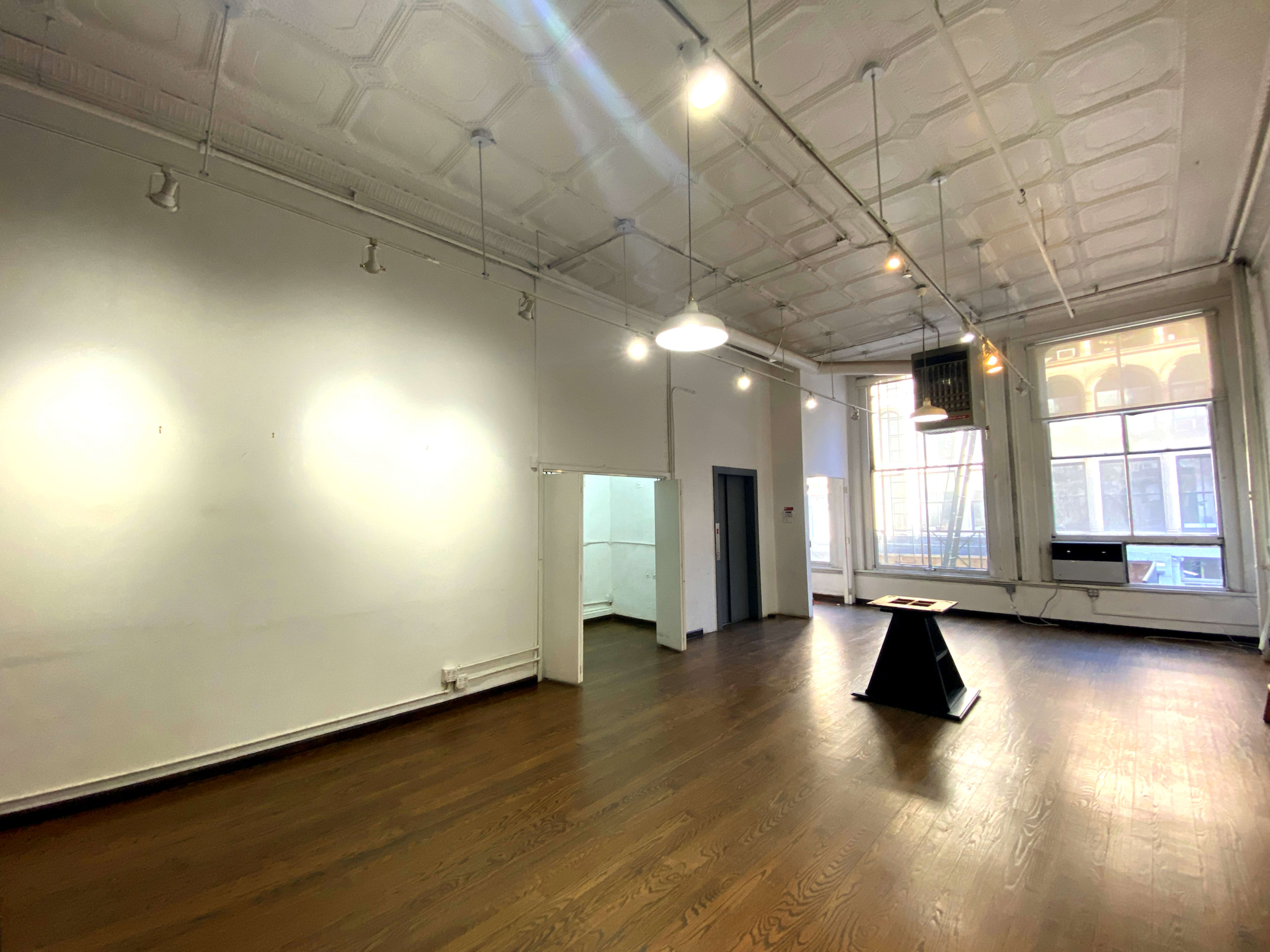 An empty room with wooden flooring, white walls, and overhead lighting fixtures.