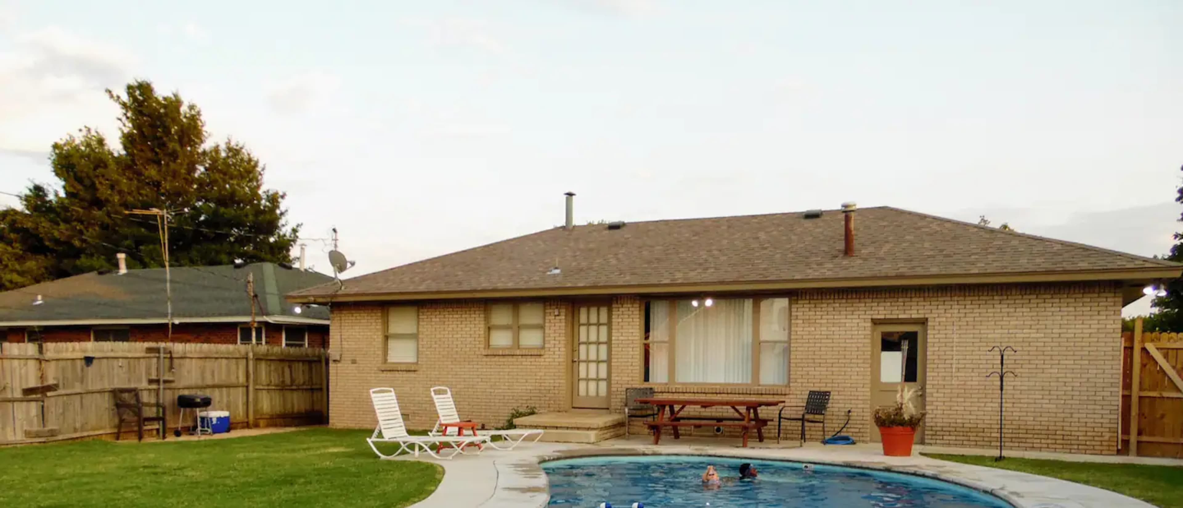 A backyard with a swimming pool, a brick house, and several lounge chairs.