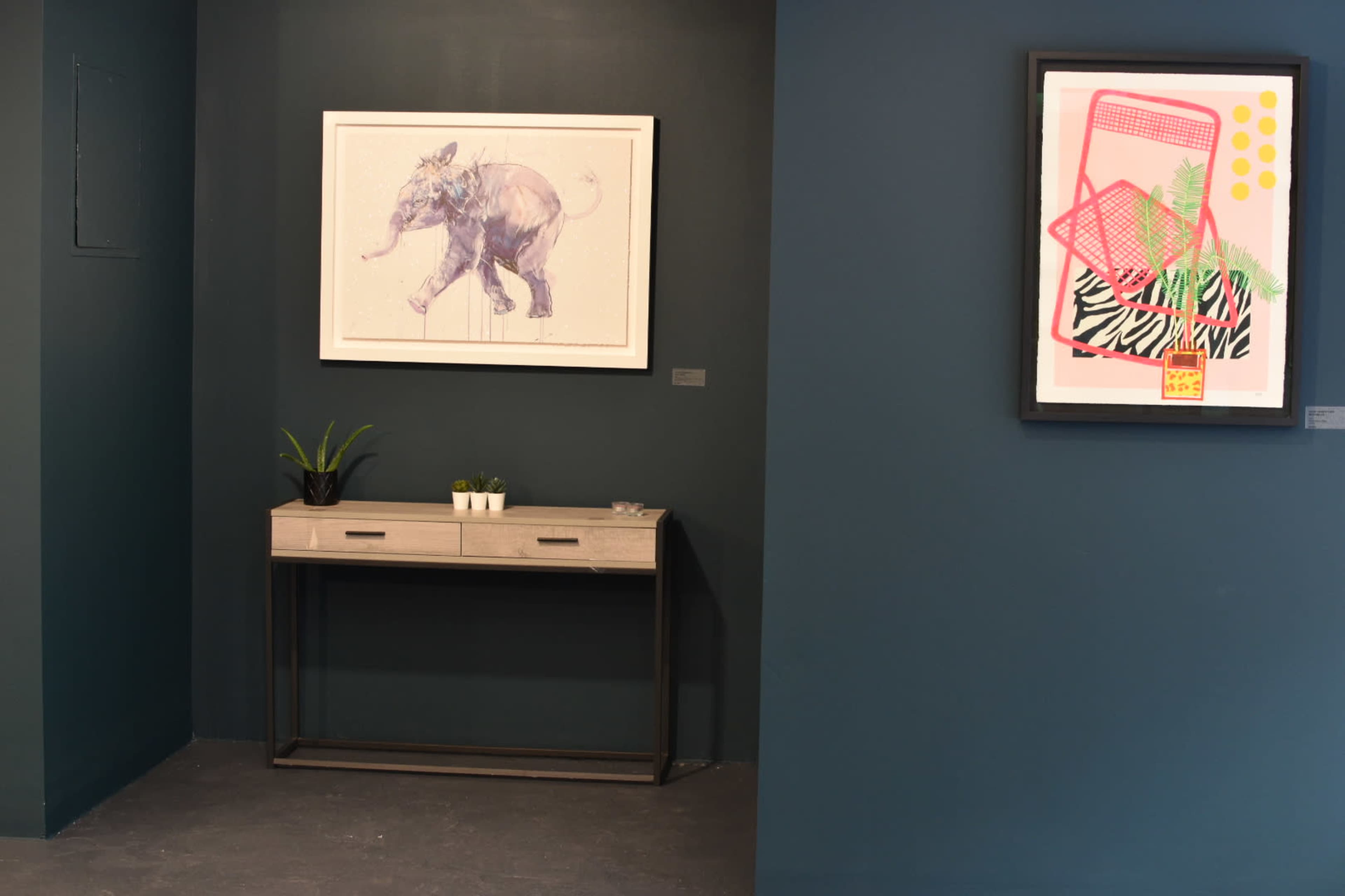 The image shows a corner of a room featuring a console table with plants and two framed artworks on contrasting dark walls.