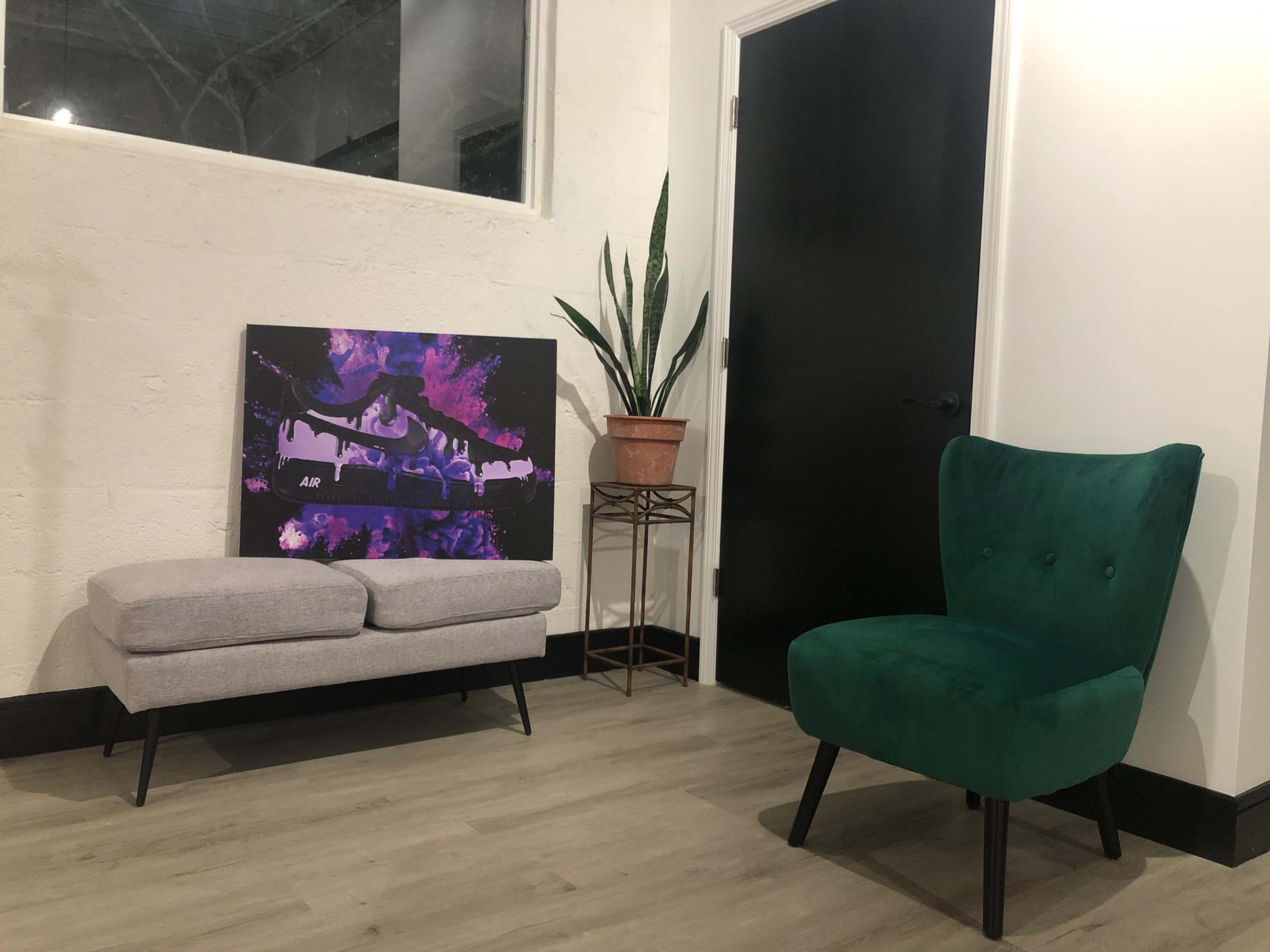A minimalist interior with a gray bench, a green chair, a potted plant, and an abstract painting on the wall.