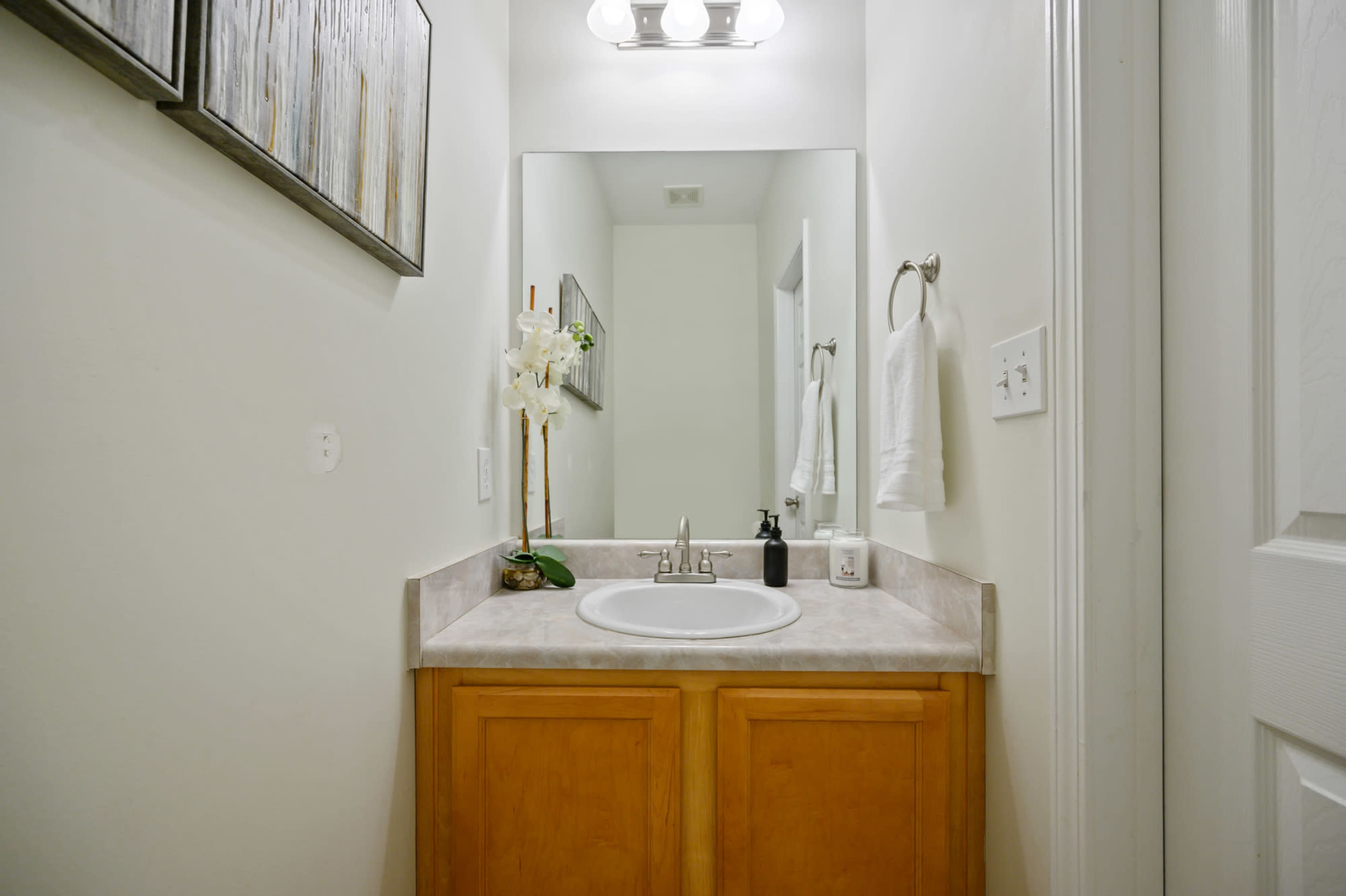 A compact bathroom with a sink, wooden cabinetry, a mirror, and decorative elements, including a potted plant and towels.