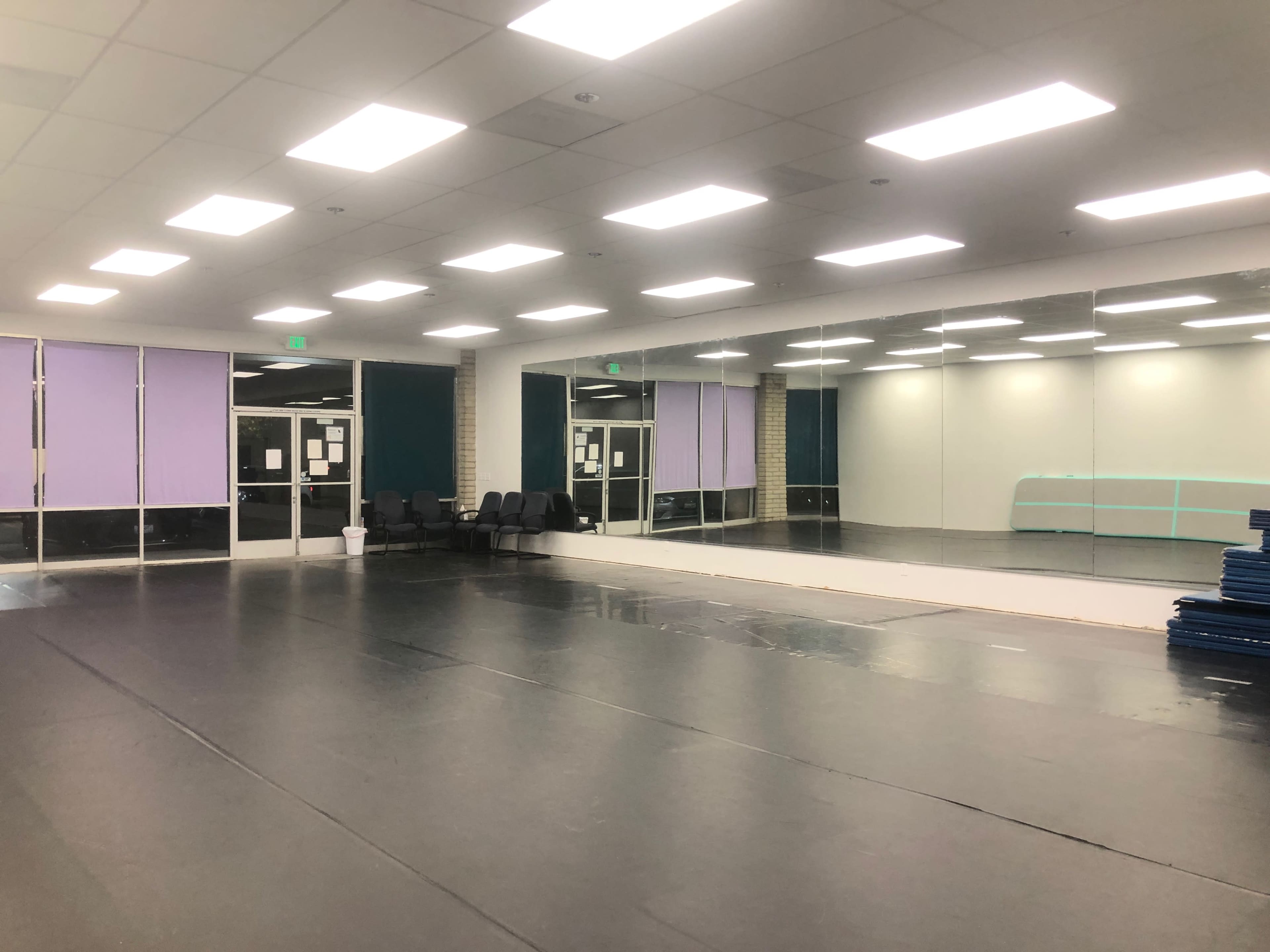 The image shows a spacious, empty dance or studio room with a mirrored wall and seating area.