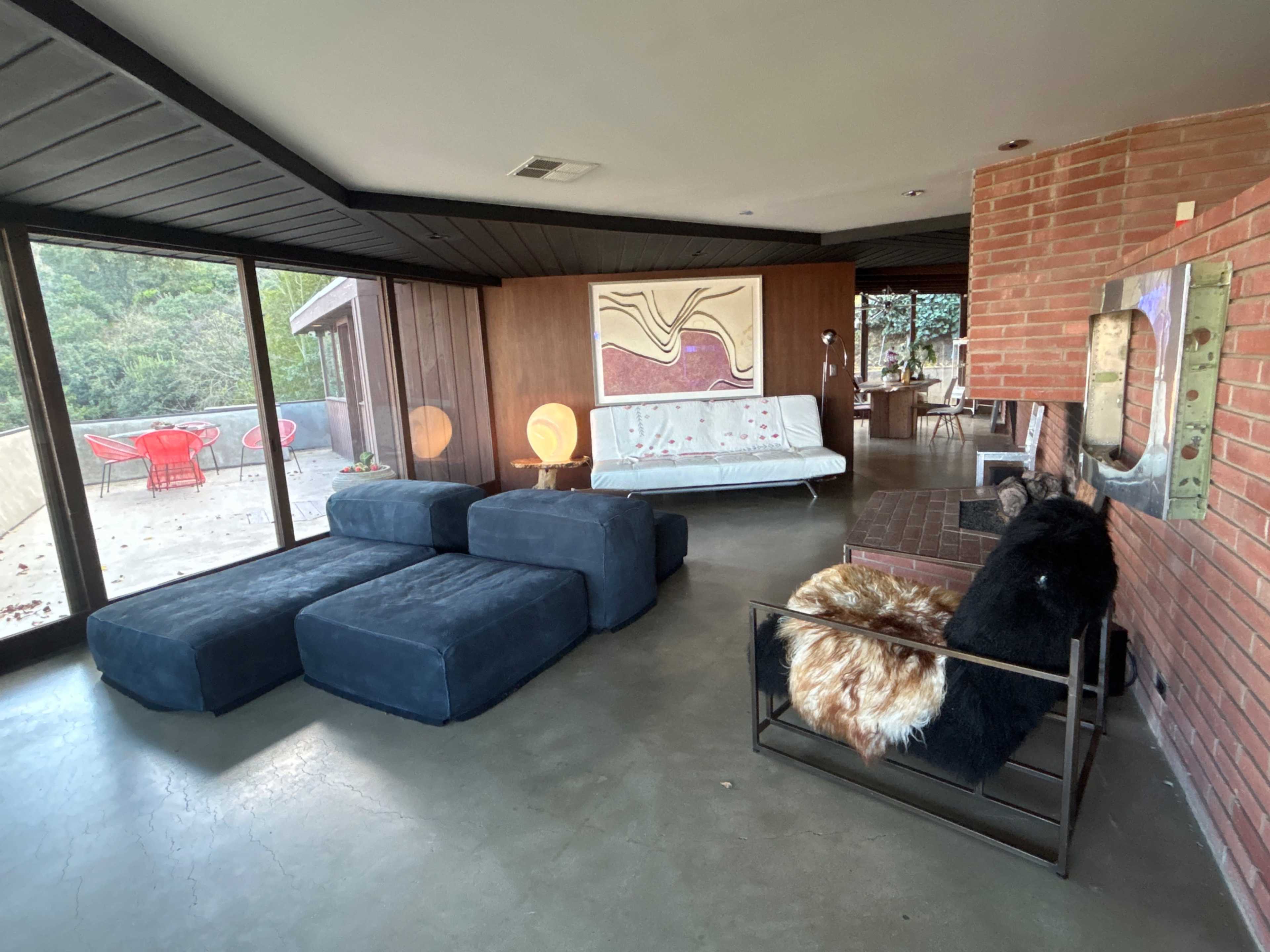 A modern interior space featuring a combination of blue seating, a wooden wall, large windows, and various furniture pieces including a sofa and a fireplace.