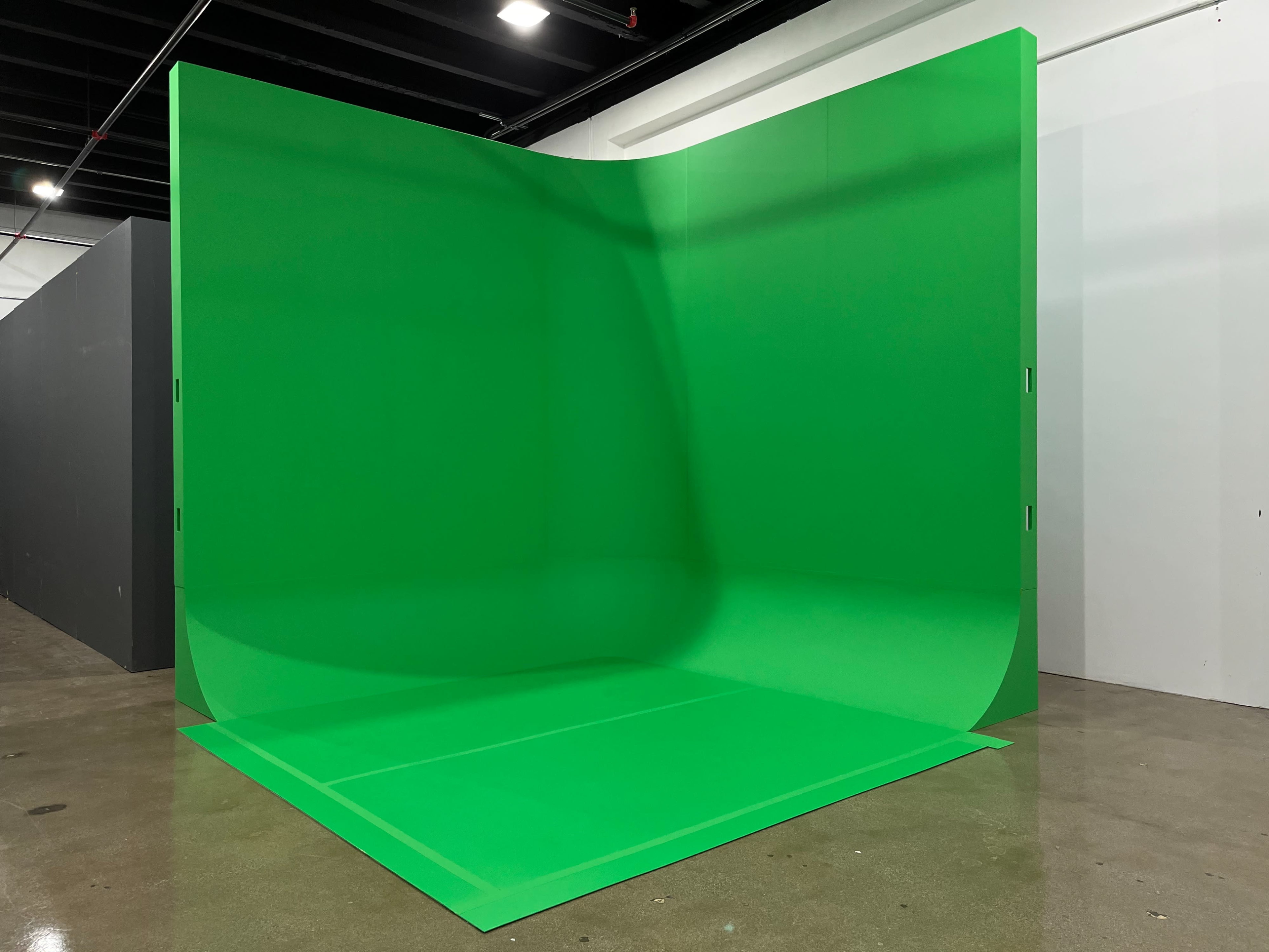 The image shows a large green backdrop set up in a studio space, designed for video or photography.