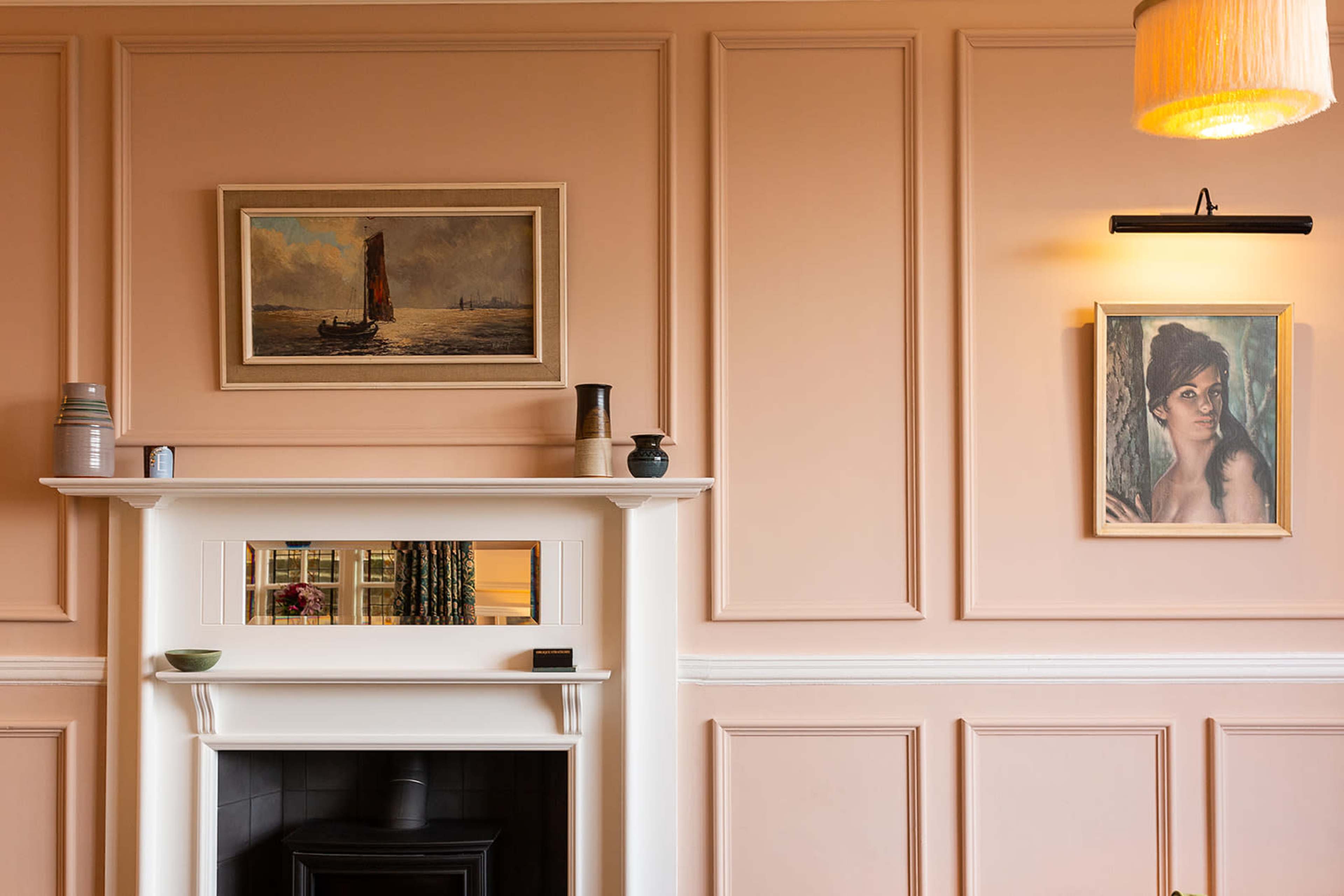 A softly painted wall with a fireplace, framed artwork, and decorative vases arranged on a shelf above the mantel.