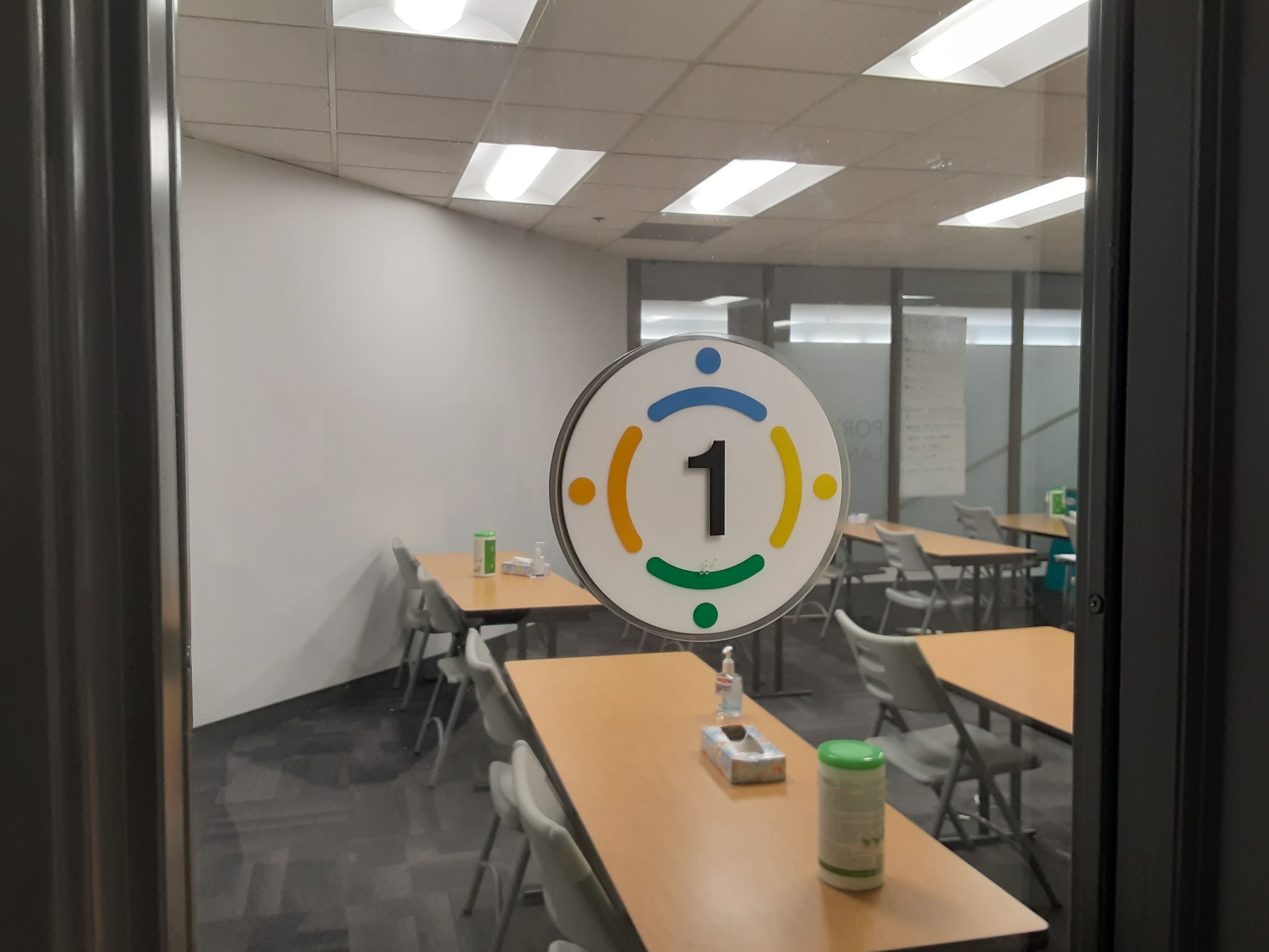 A circular sign displaying the number "1" is affixed to a glass door, leading into a meeting room with tables and chairs arranged inside.