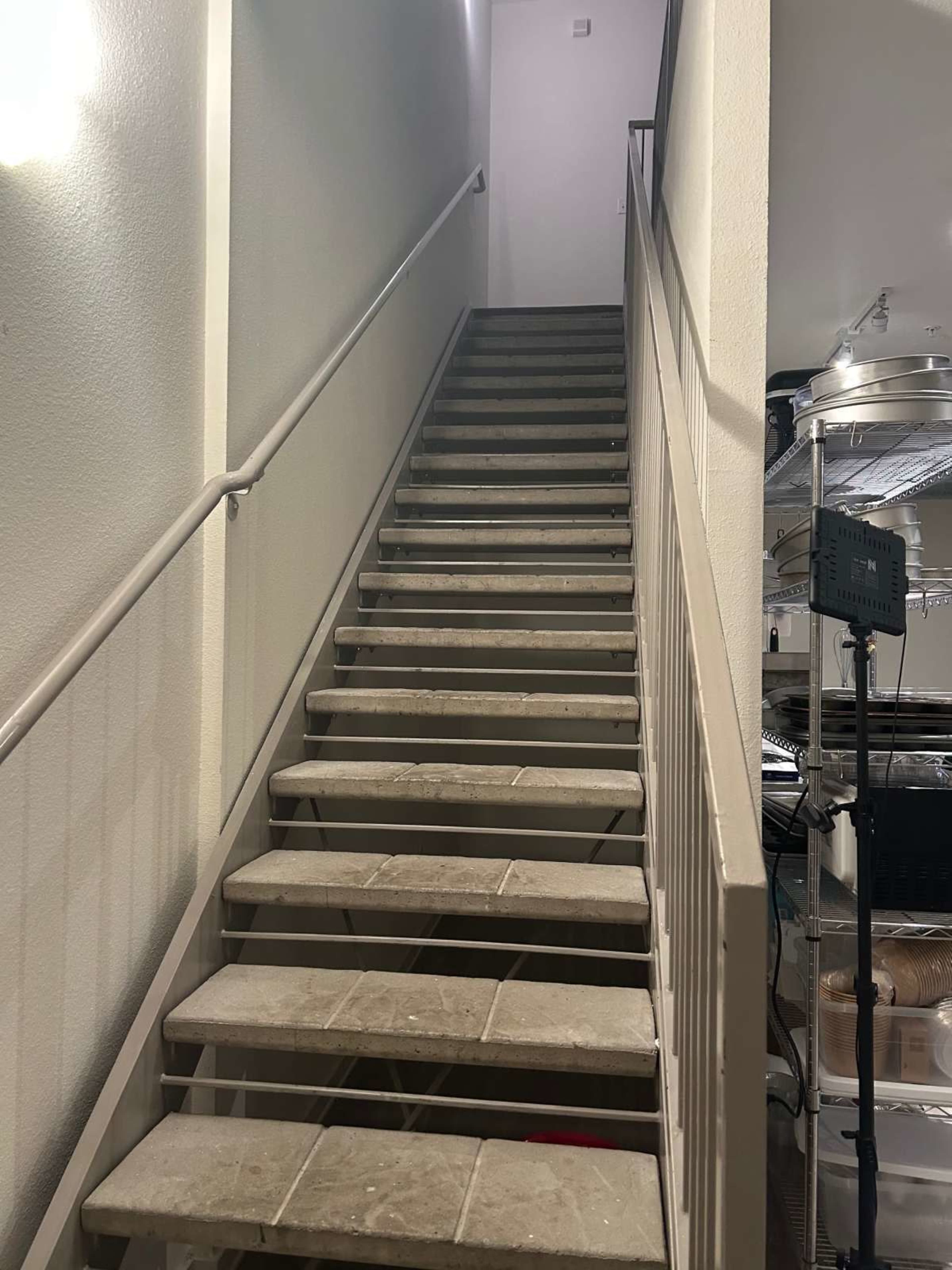 A set of stairs leads upward to a landing, with a plain white wall on one side and a railing along the other.