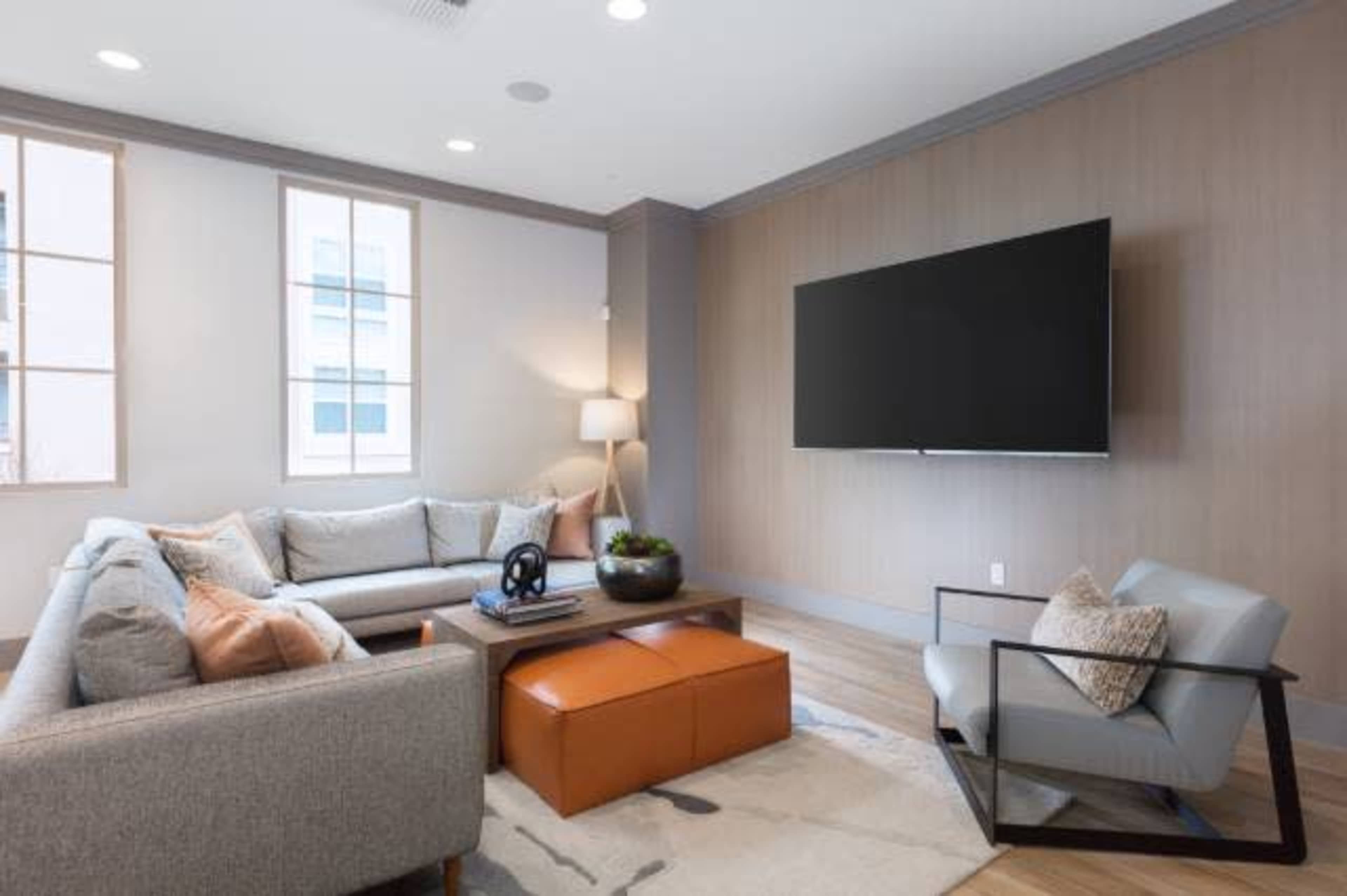 A modern living room featuring a gray sofa, an orange ottoman, a coffee table, and a wall-mounted television.
