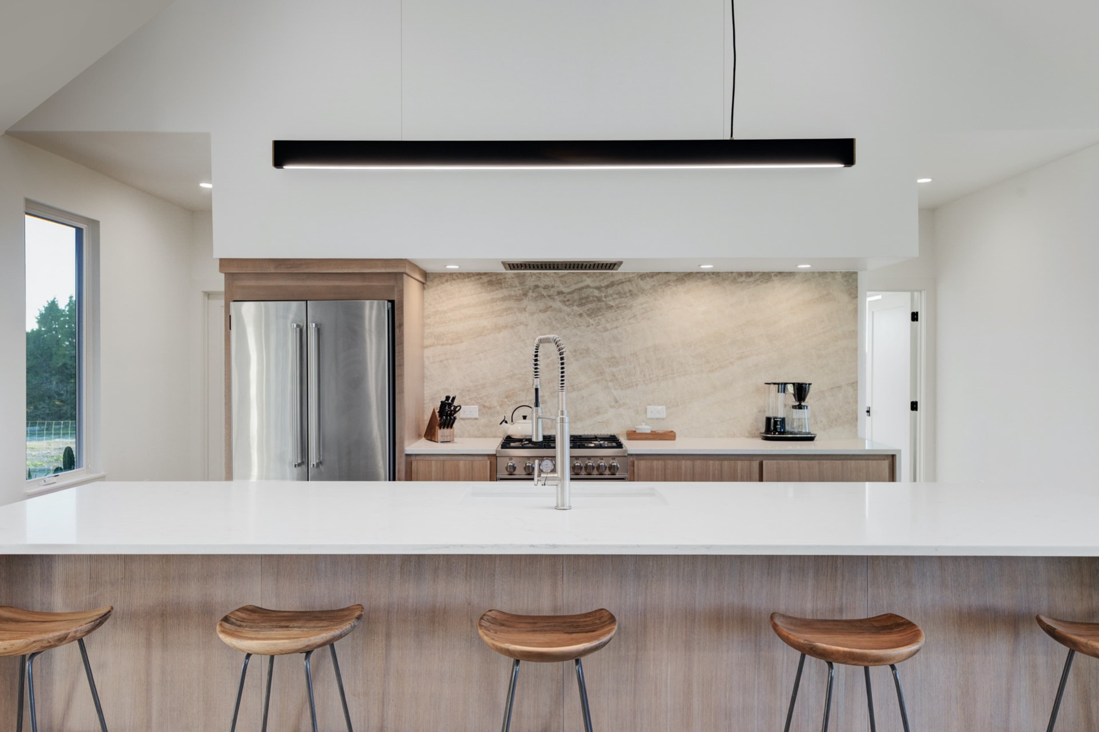 A modern kitchen with a large island, bar stools, and sleek appliances, set against a textured stone backsplash.