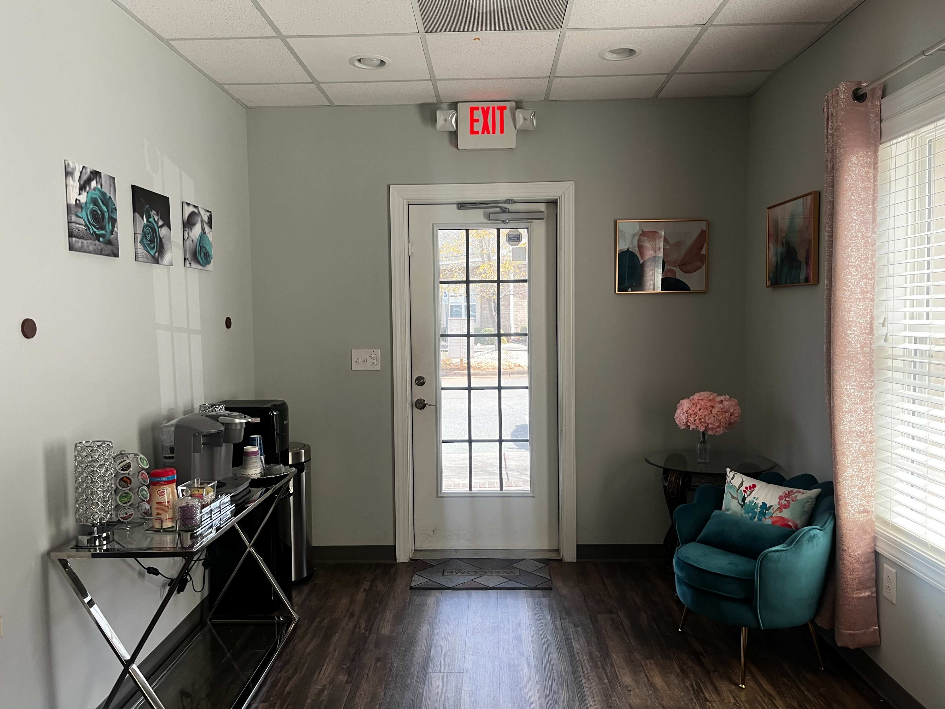 A small reception area with a door leading outside, a green armchair, a console table with various items, and wall decorations including framed pictures.