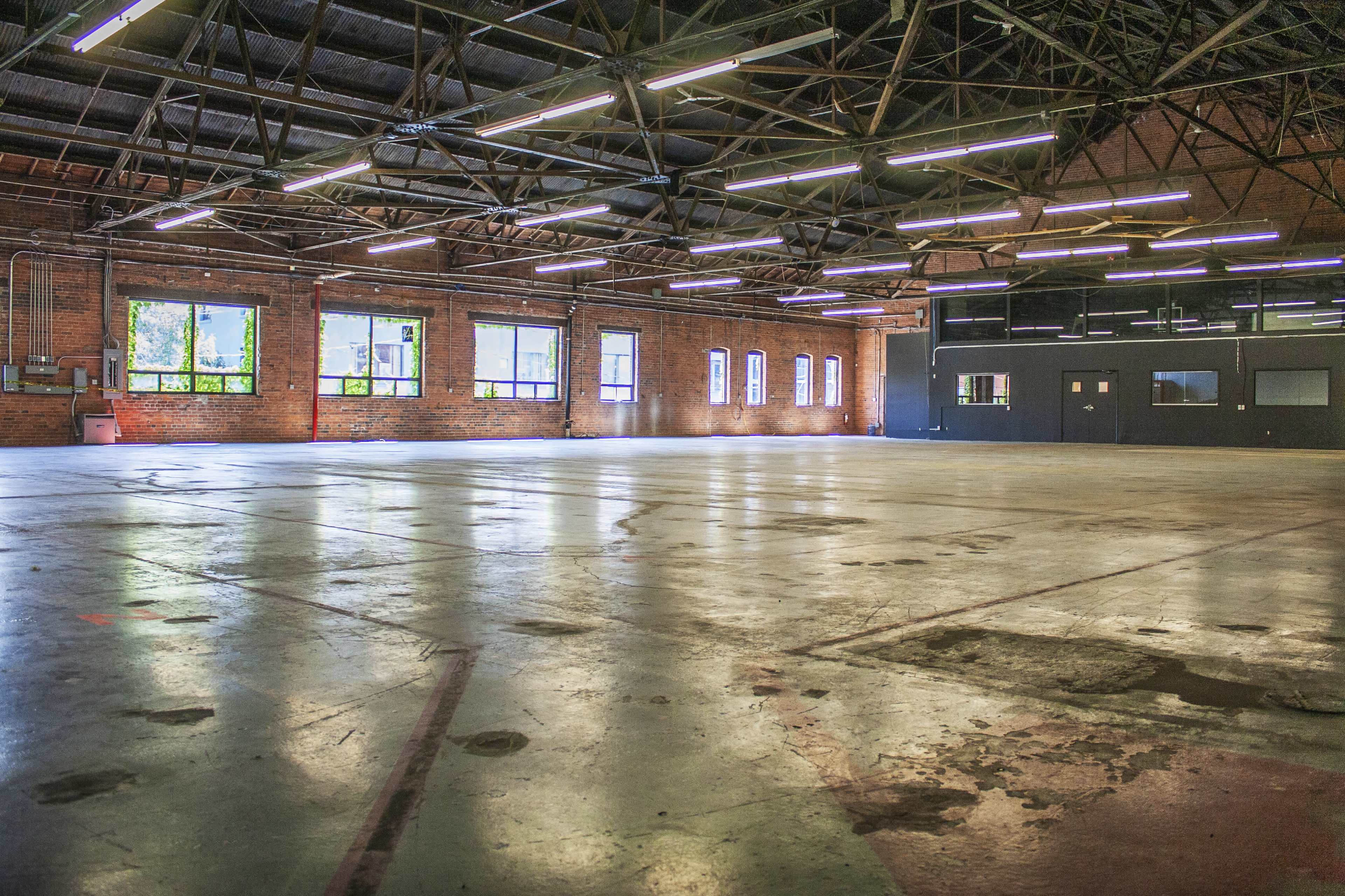 A large, empty industrial space with exposed brick walls, large windows, and a polished concrete floor.