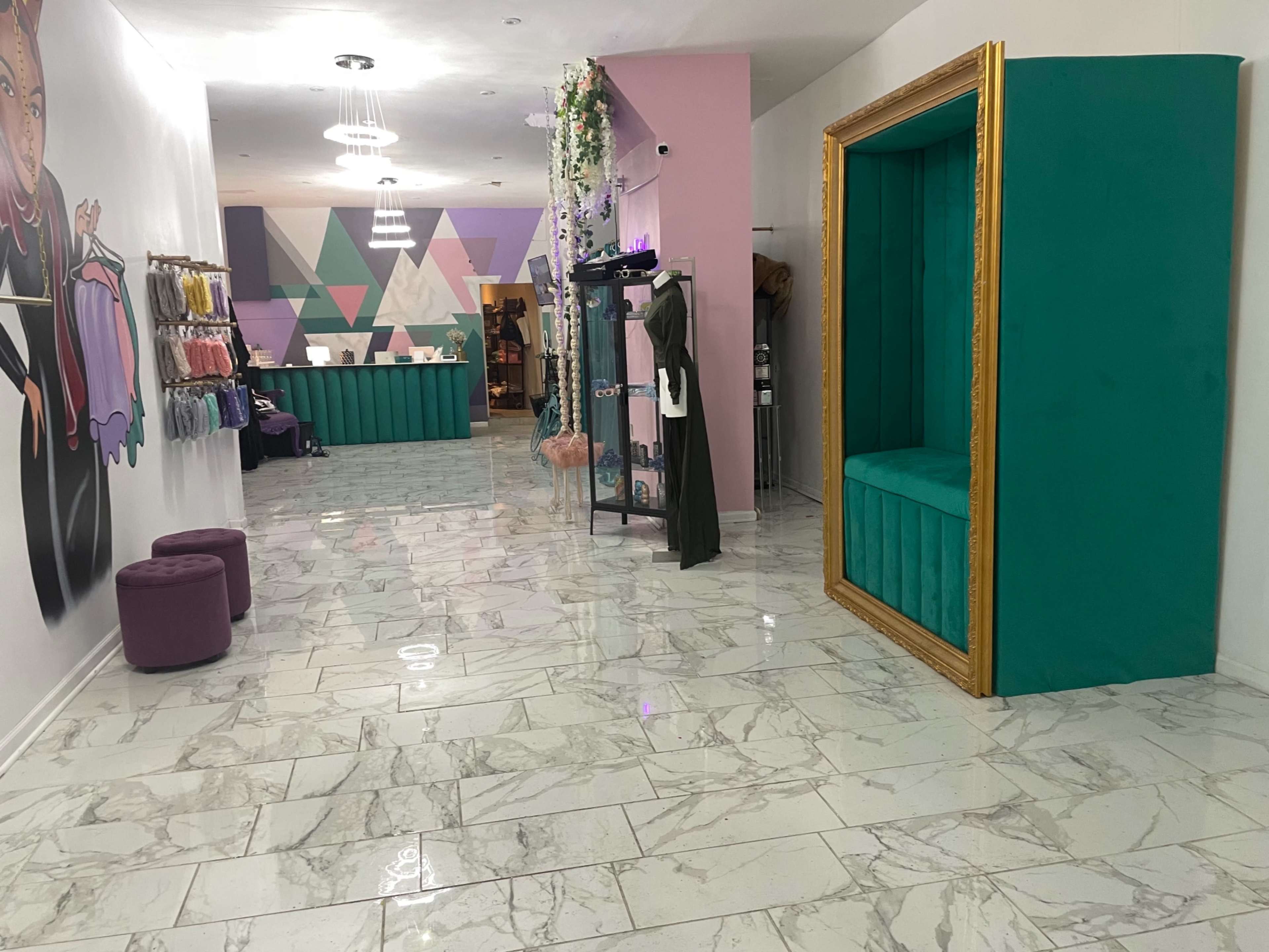 A brightly lit boutique interior with marble flooring, teal and pink walls, and a decorative seating area framed in gold.