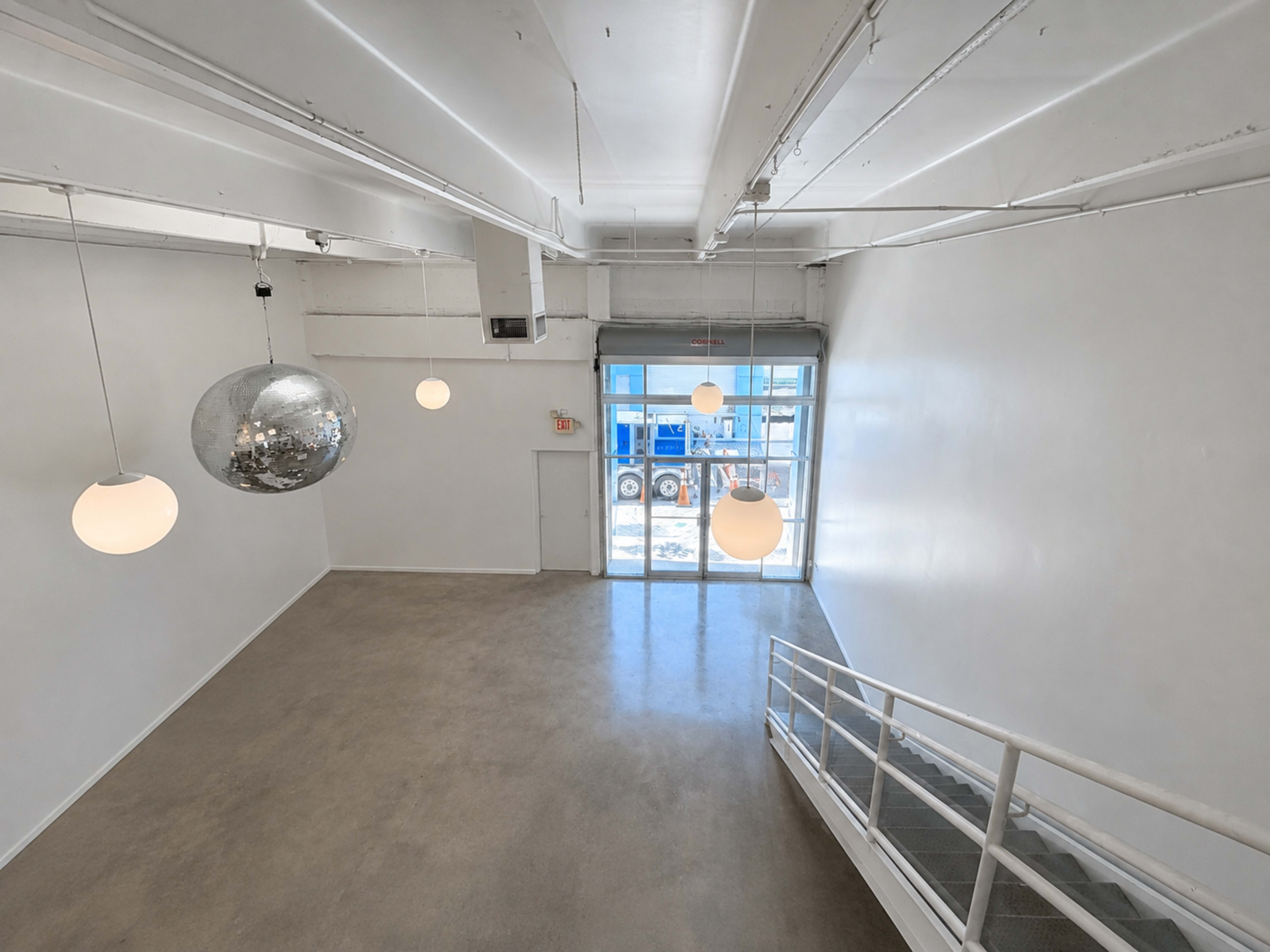The image shows a spacious, brightly lit interior room with a staircase, large windows, and pendant lights, including a disco ball.