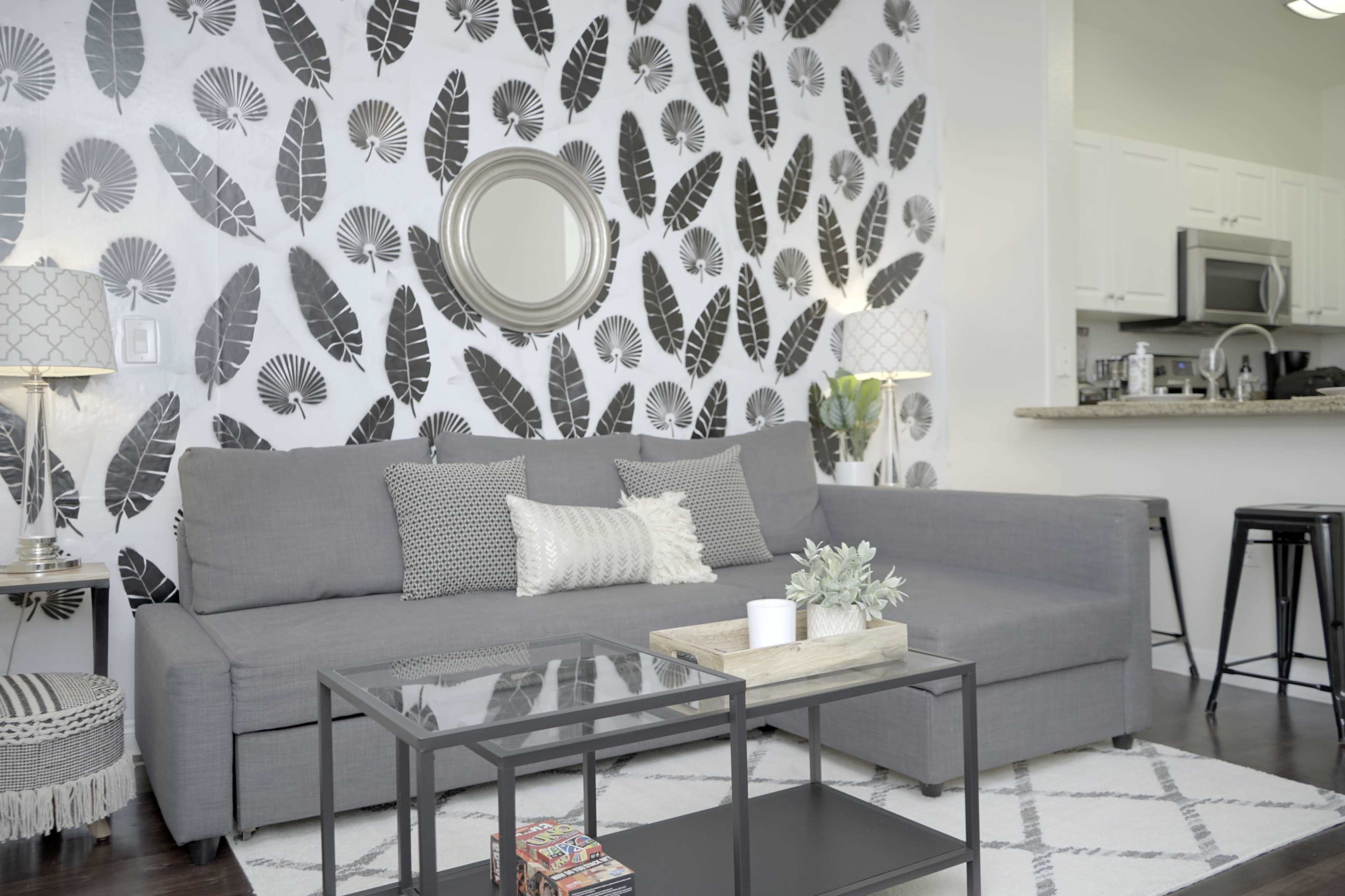 The living room features a gray sofa against a leaf-patterned accent wall, with a coffee table and decorative items in the center.