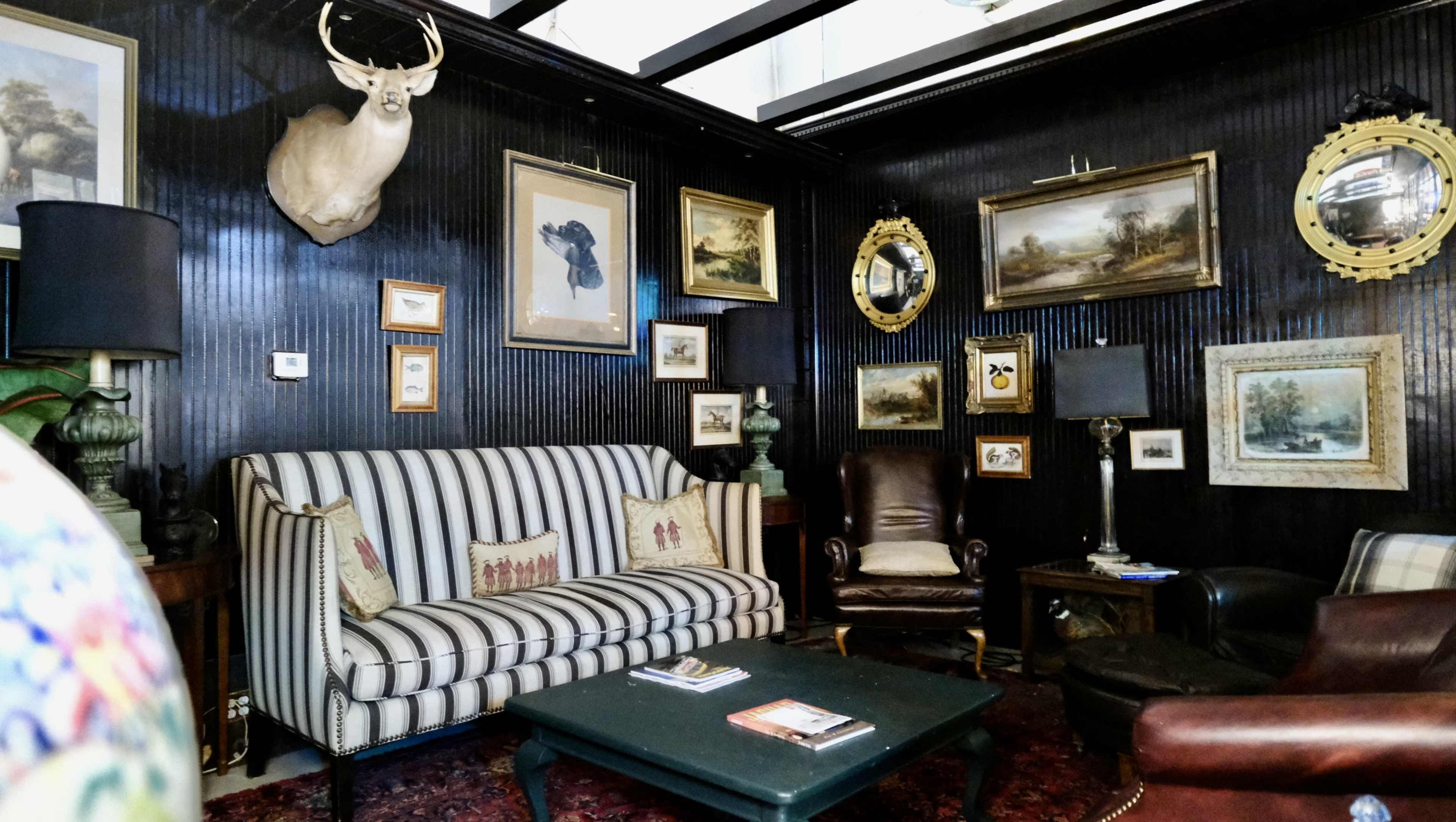 A cozy room featuring a striped sofa, leather armchairs, and a wall adorned with various framed artworks and decorative mirrors.