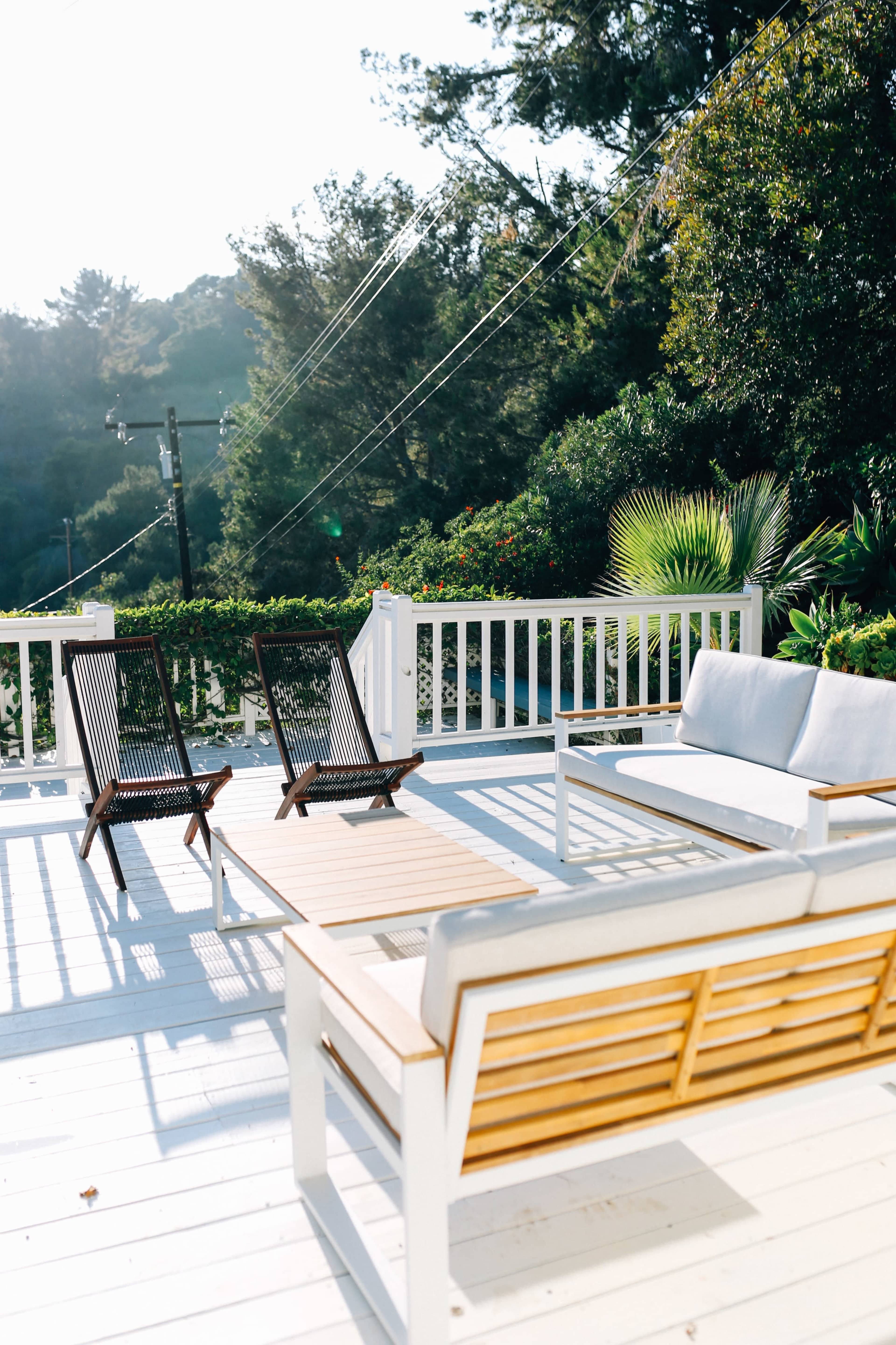 A deck features a wooden table and chairs, with two lounge chairs positioned nearby under a clear sky.