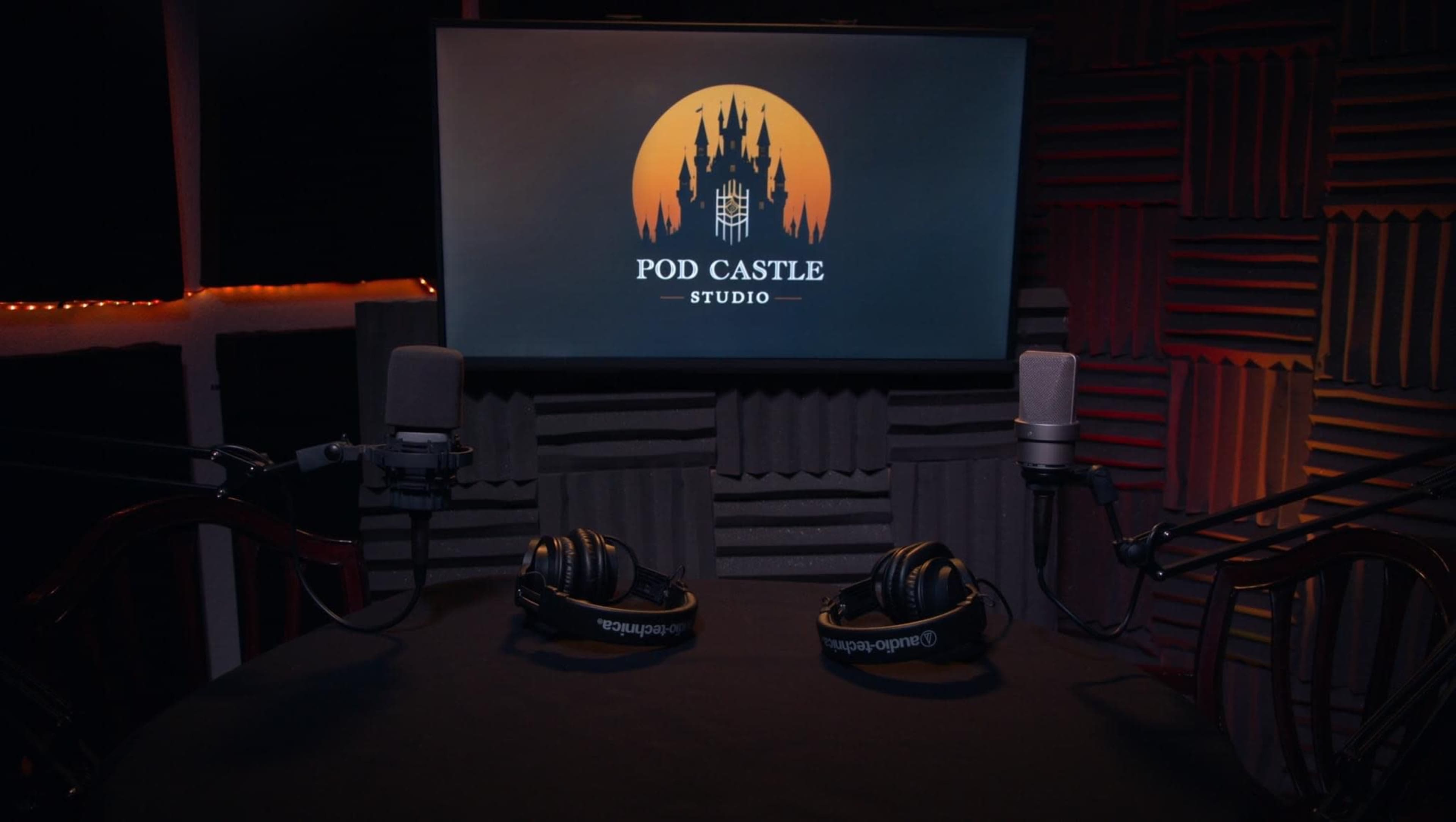 A soundproof podcast studio features two microphones, headphones, and a monitor displaying the "Pod Castle Studio" logo against a backdrop of a castle silhouette.