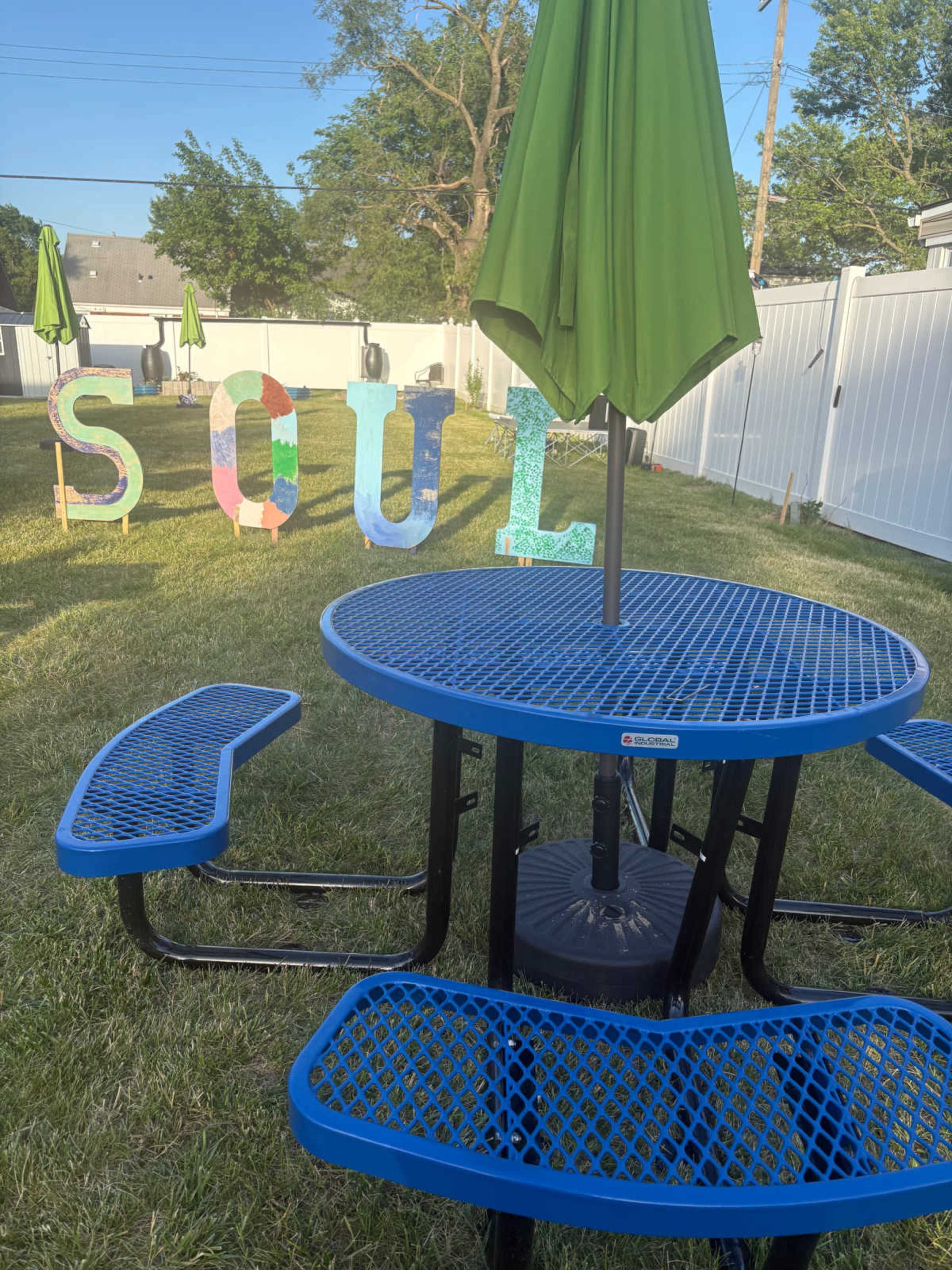 A blue picnic table with attached benches is set in a grassy area, next to colorful letters spelling "SOUL."