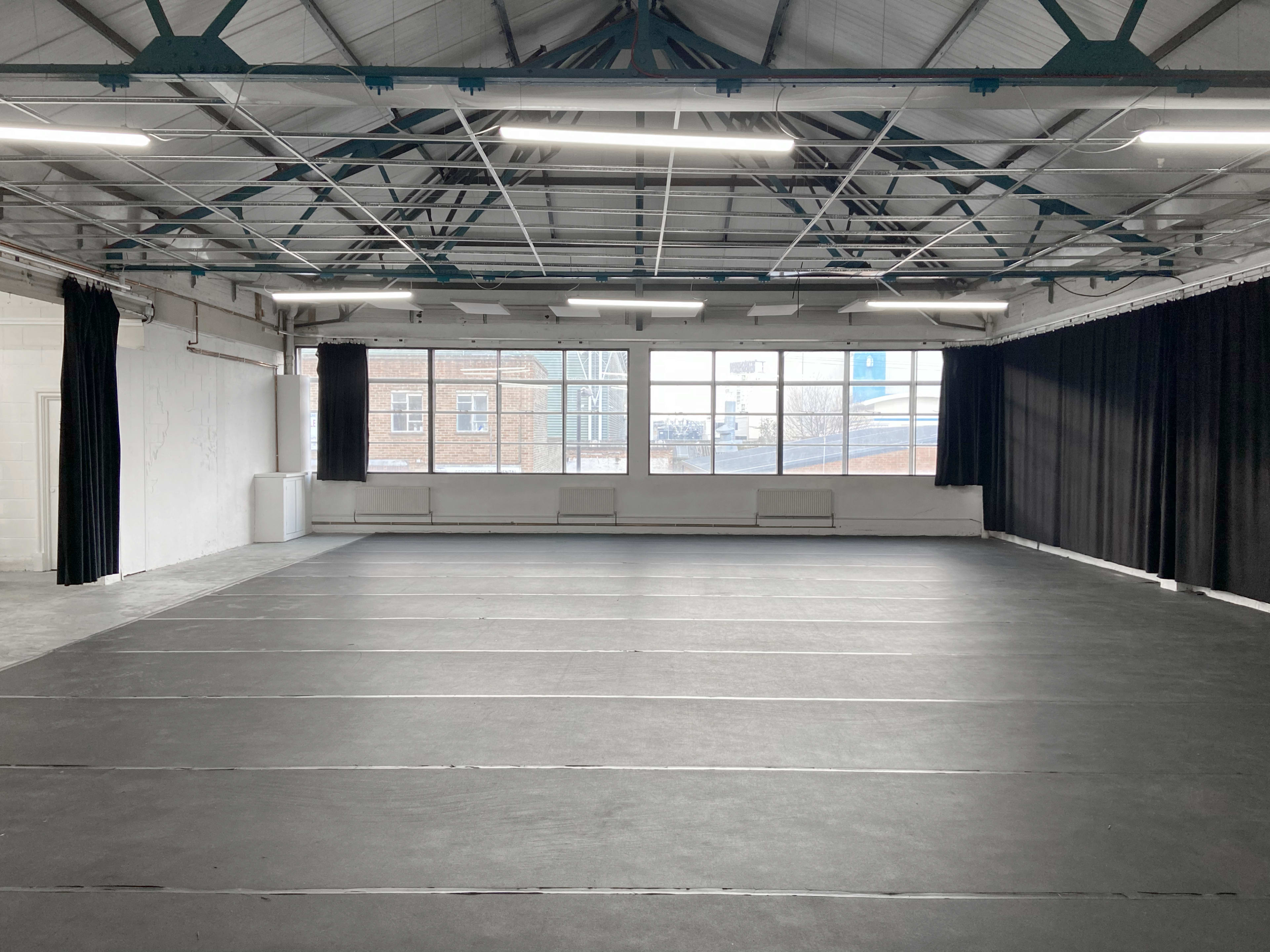 A spacious, empty studio with a black mat flooring and large windows providing natural light.