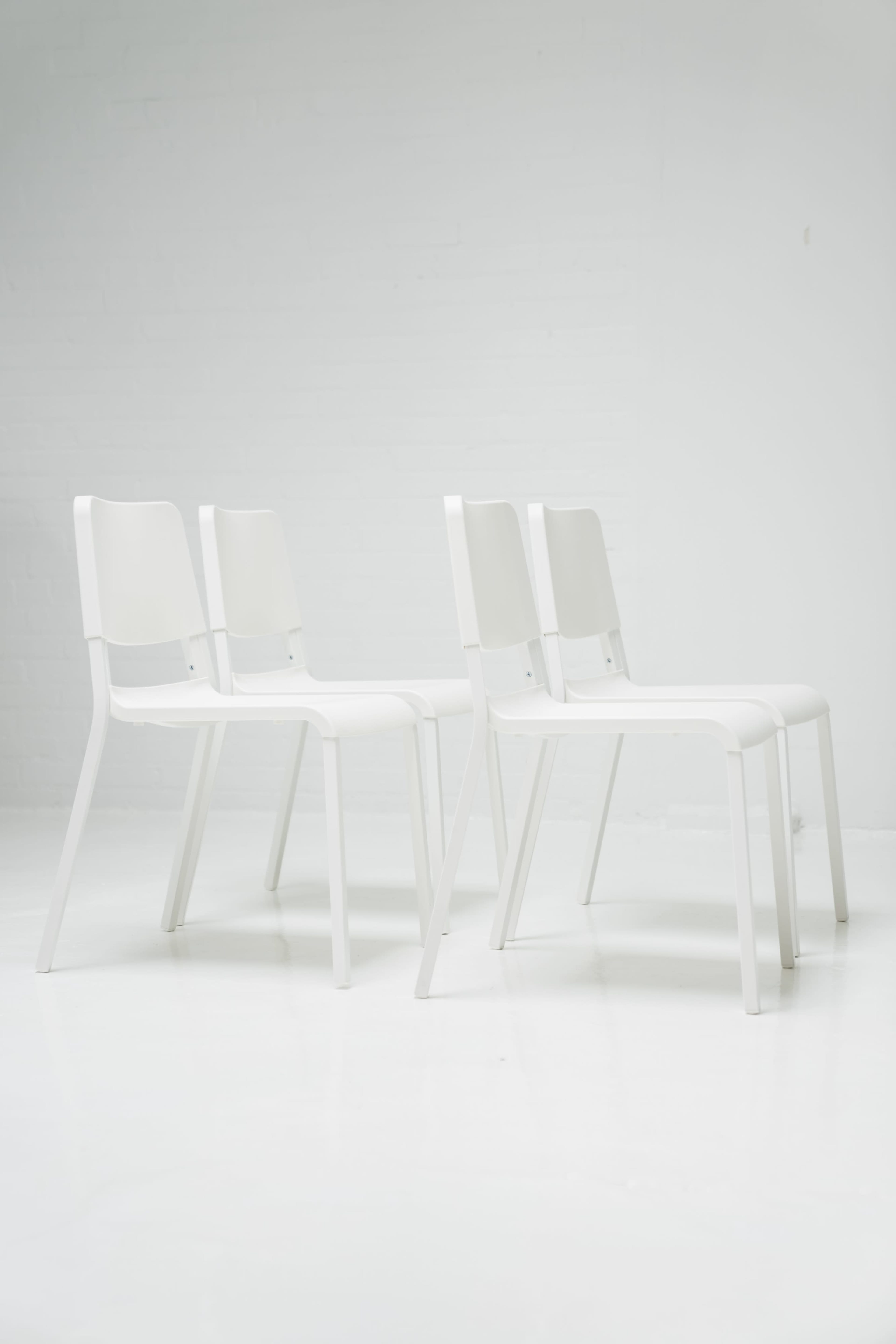 Three white chairs are arranged in a minimalist manner against a plain white background.