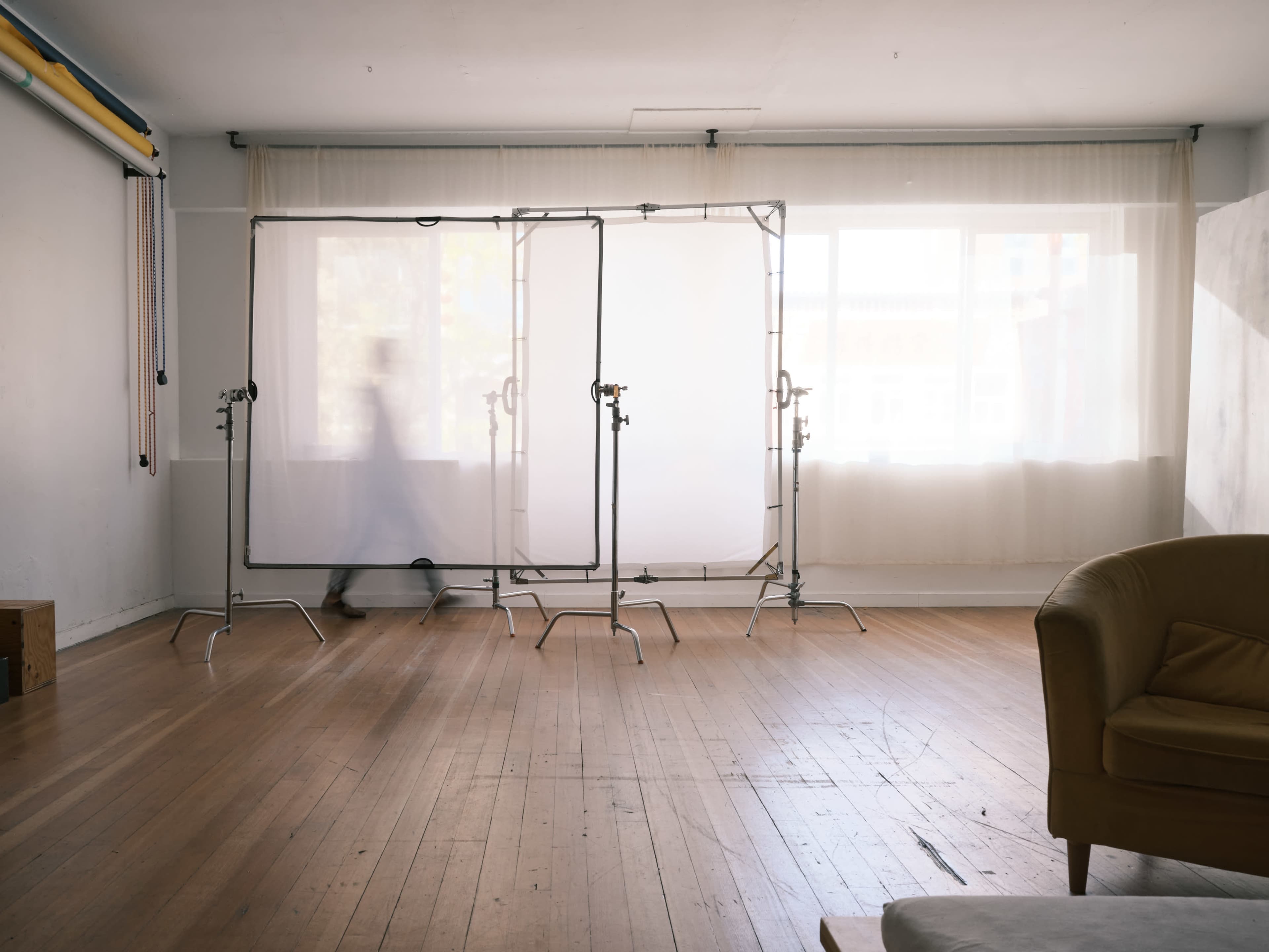 A person walks past light-diffusing panels in a spacious, sunlit studio with wooden floors.