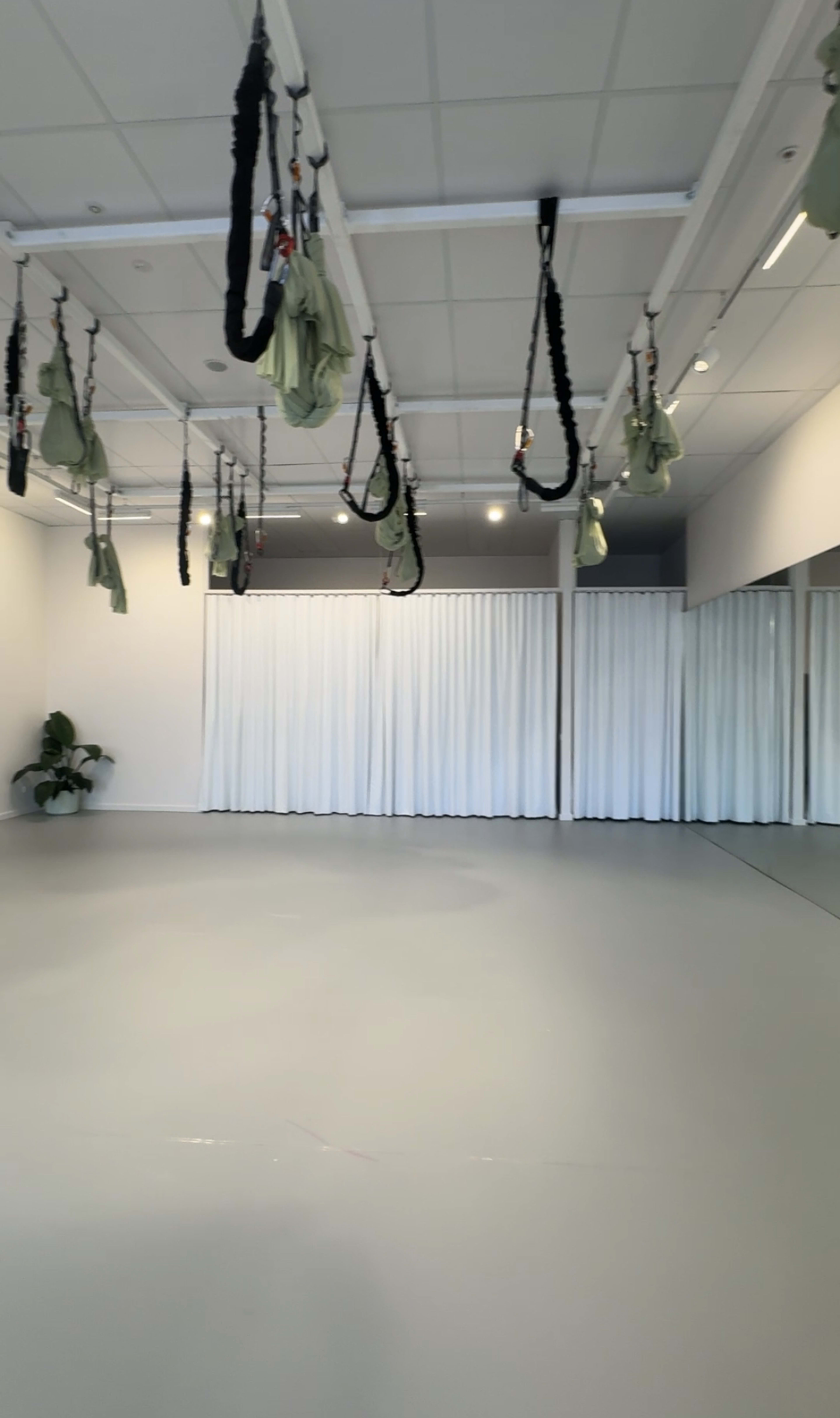 The image shows a spacious, minimalist studio with suspended fabric hammocks and a large mirrored wall.