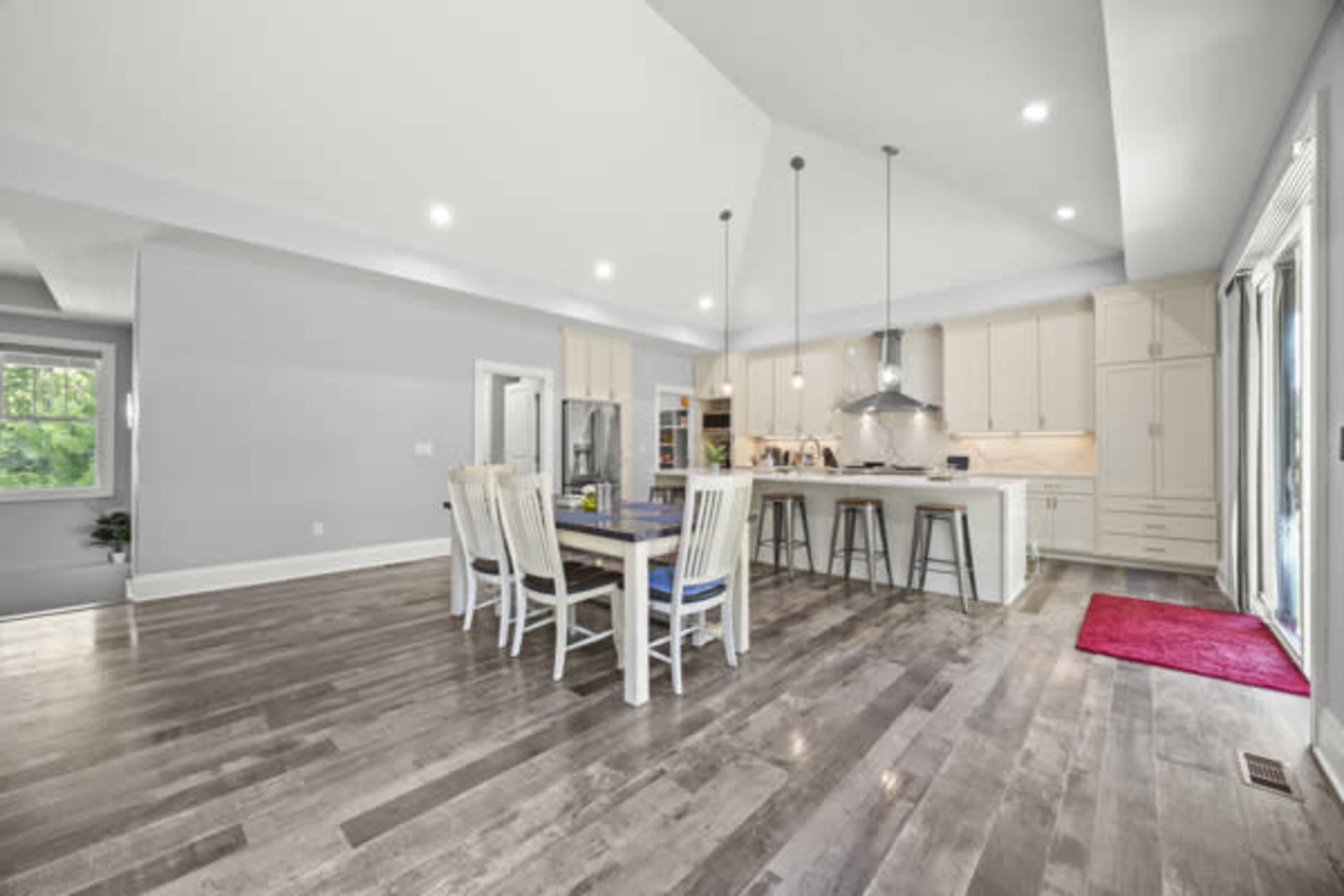 A modern kitchen and dining area feature a large table surrounded by white chairs, with a central island and stainless steel appliances.