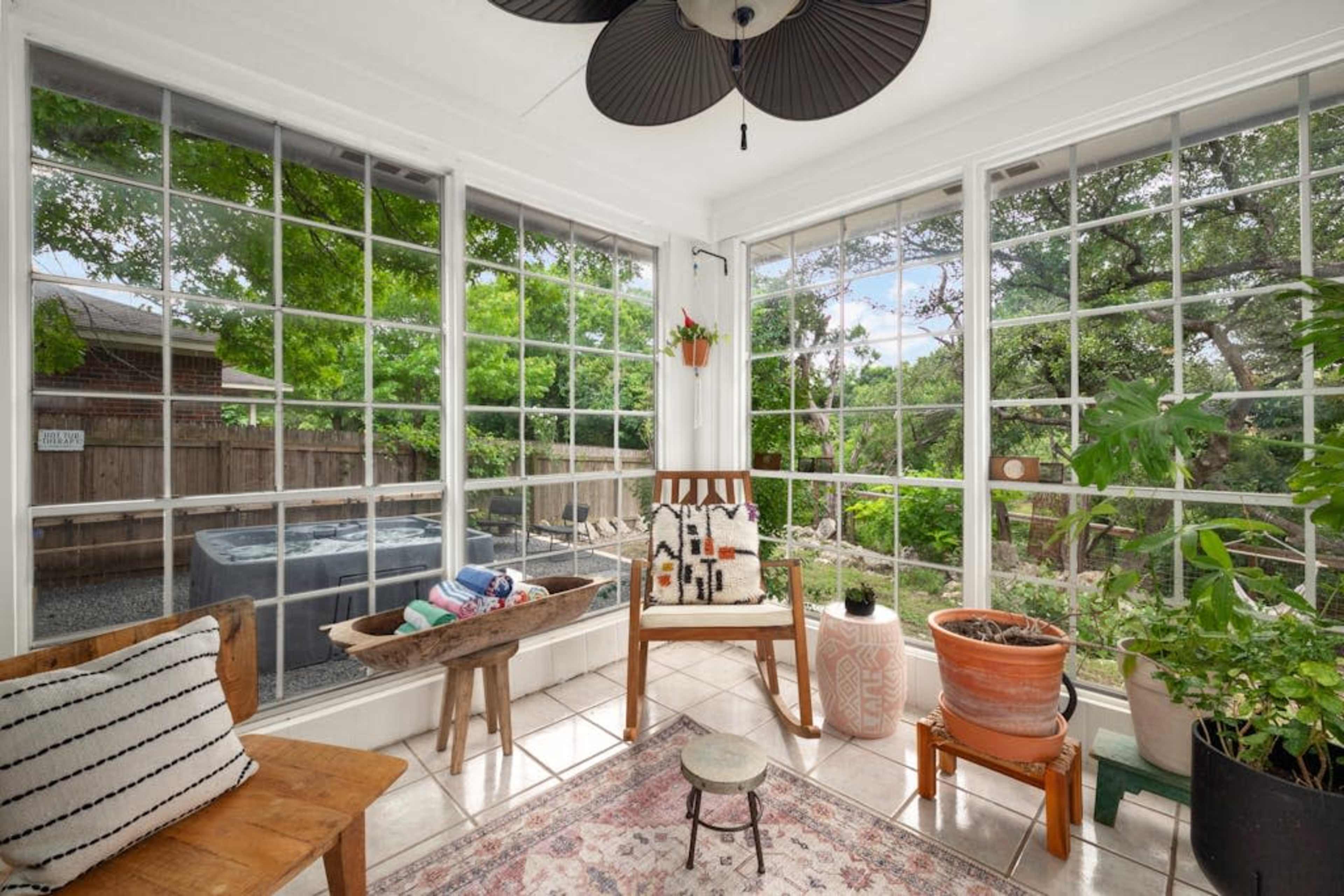 A sunlit sunroom with large windows, a chair, potted plants, and a small table.
