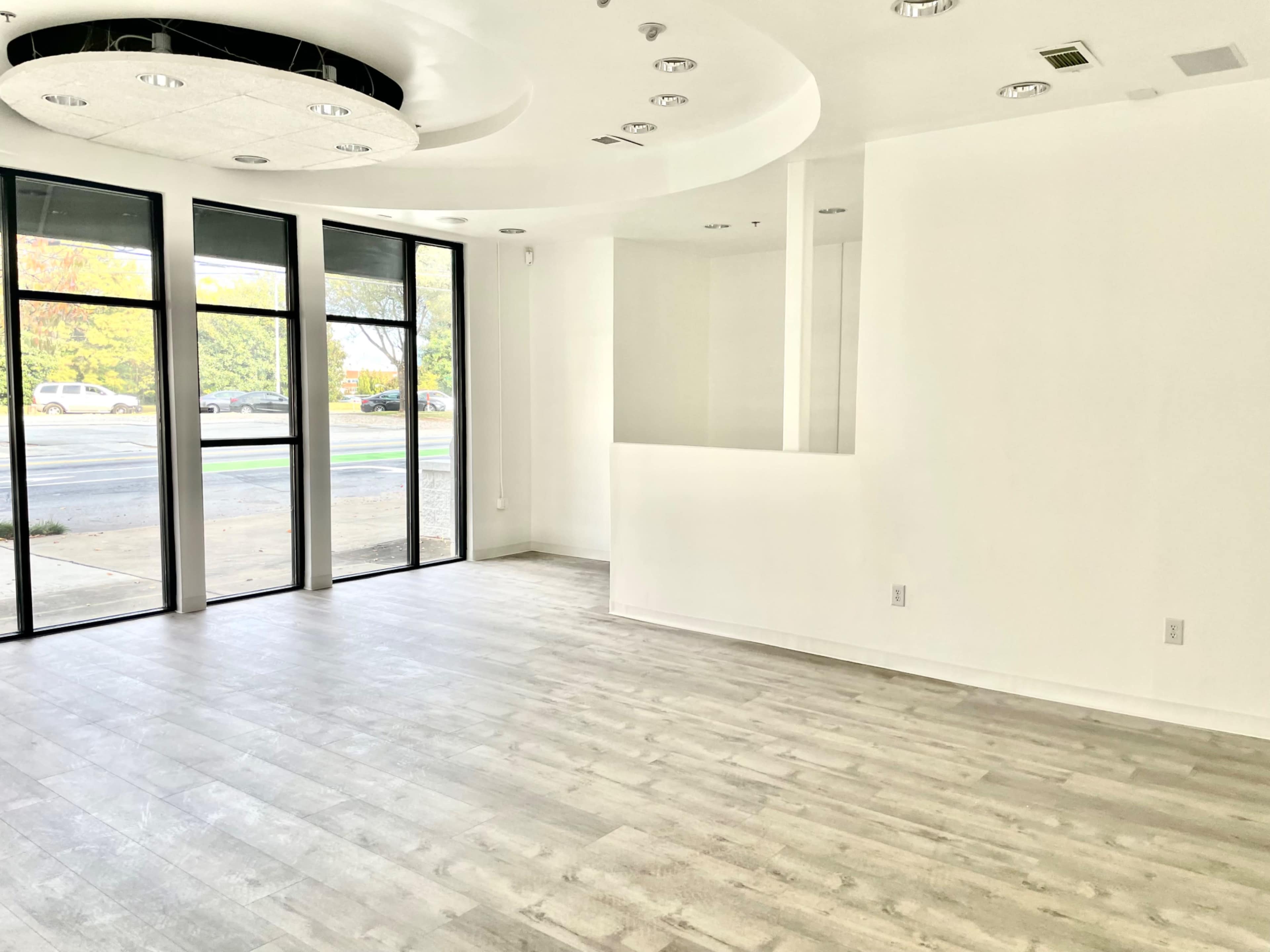 An empty room with white walls, large windows, and light-colored wooden flooring.