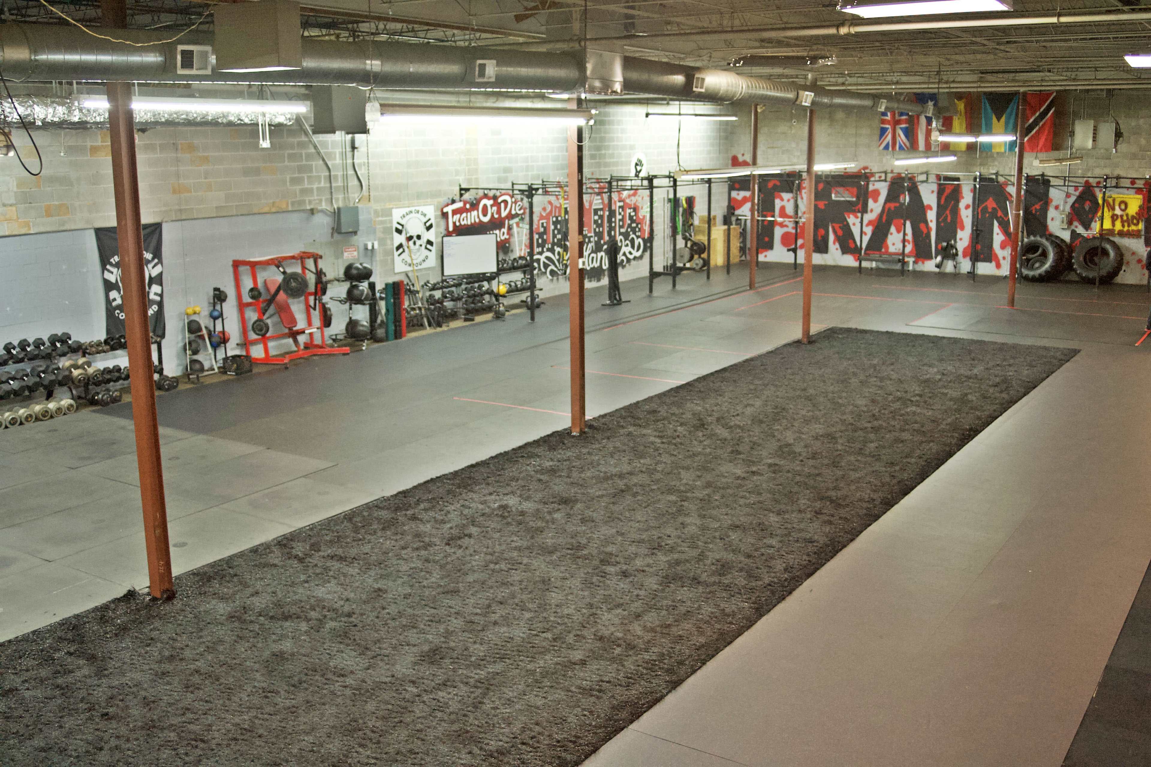 A spacious gym interior with exercise equipment, including free weights and a long turf area for workouts.