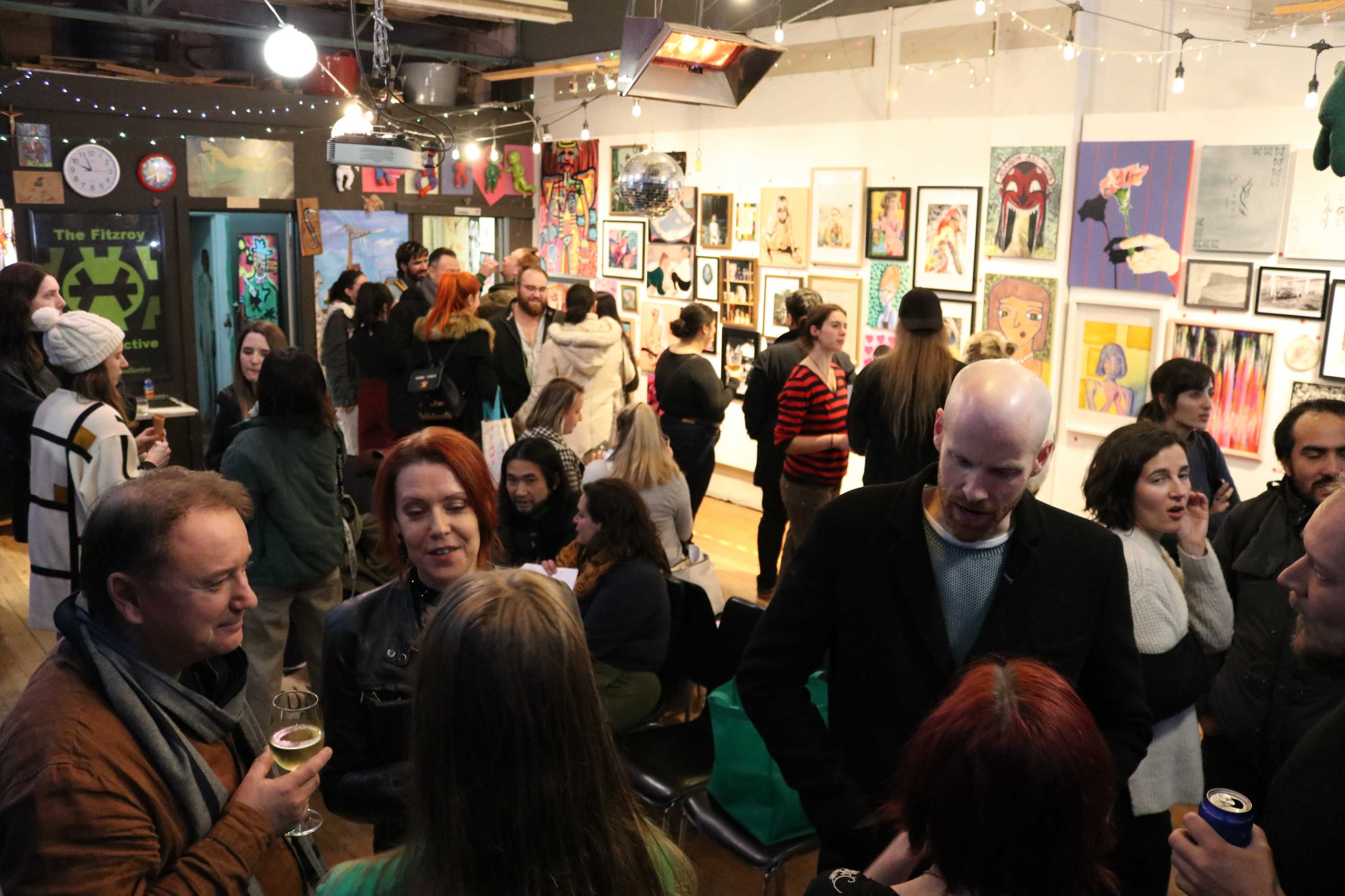 A group of people mingles in an art gallery filled with colorful artworks and various decorative lights.