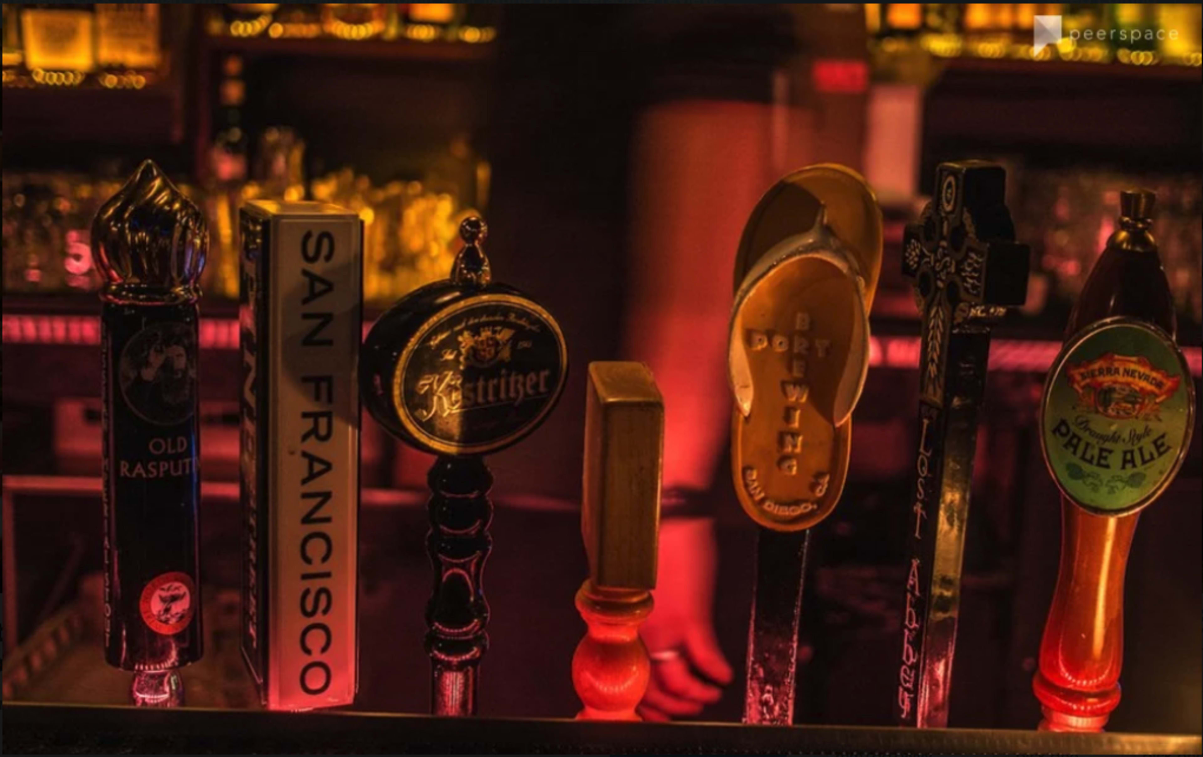 A lineup of beer taps with various labels and a single flip-flop on one of the handles.
