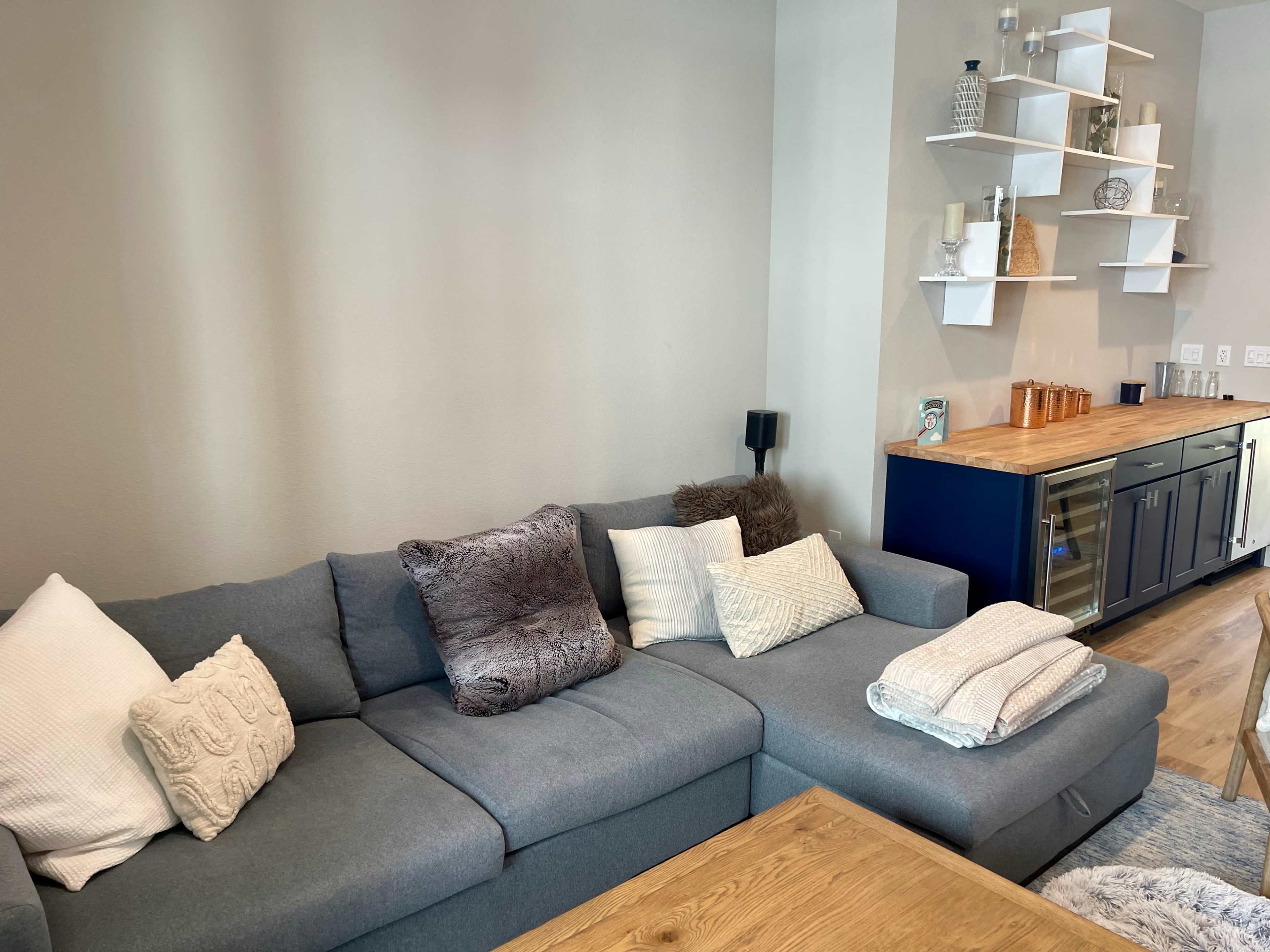 A modern living room featuring a gray sectional sofa with decorative pillows, a wooden coffee table, and a bar cabinet against the wall adorned with various items.