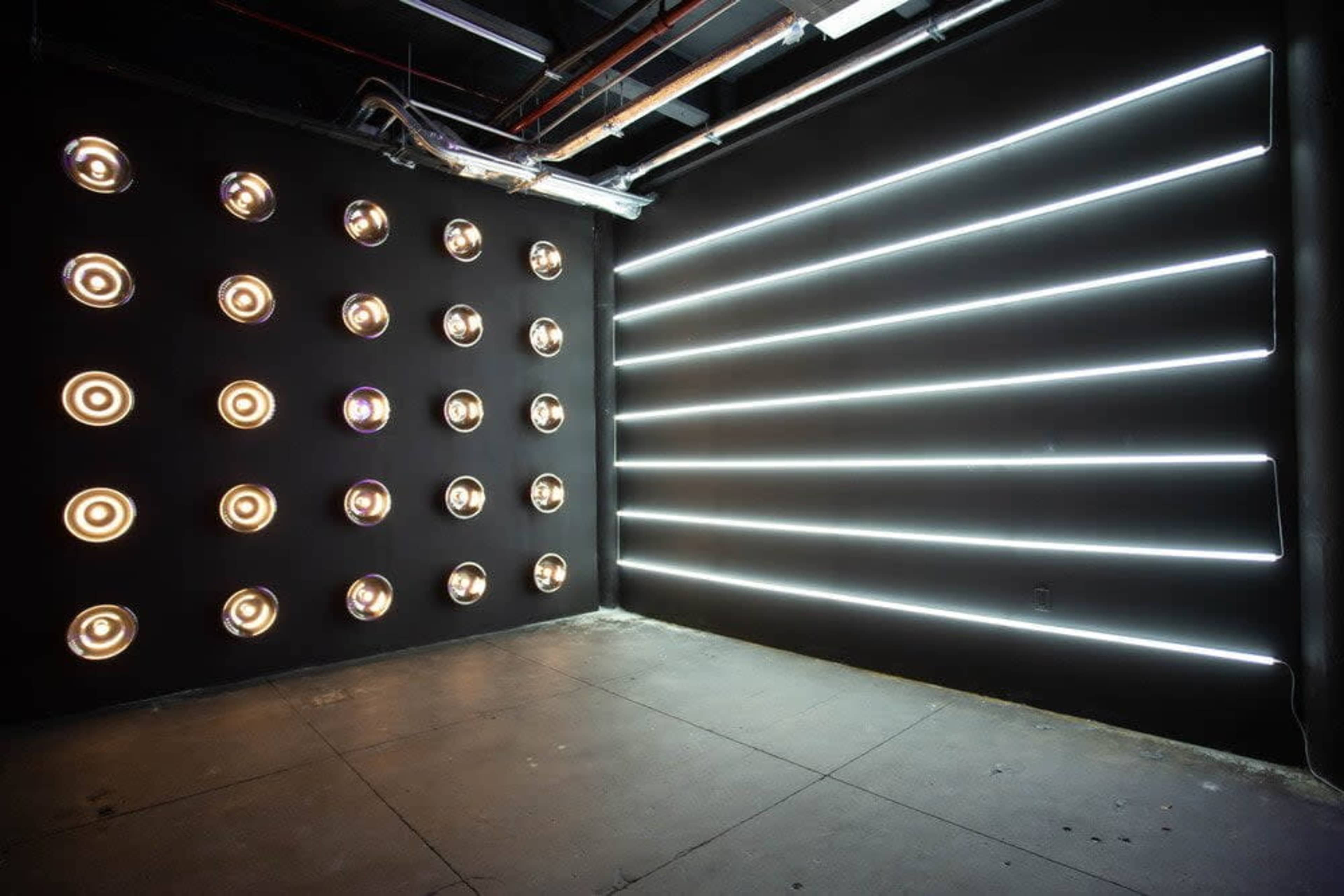 The image shows a dark room with a wall adorned with circular light fixtures and another wall featuring horizontal LED light strips.